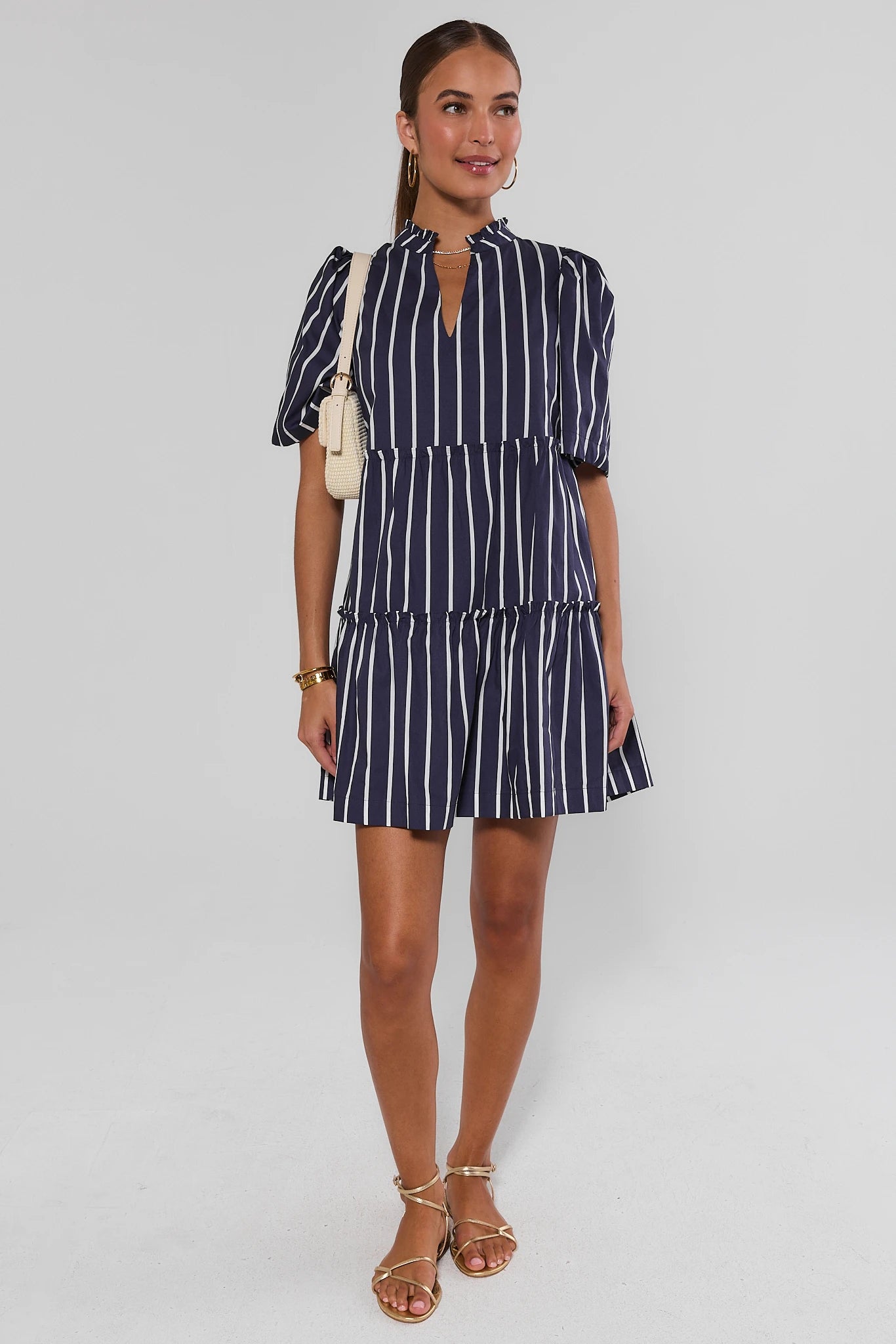 Woman wearing a navy and white striped dress on a light gray background standing
