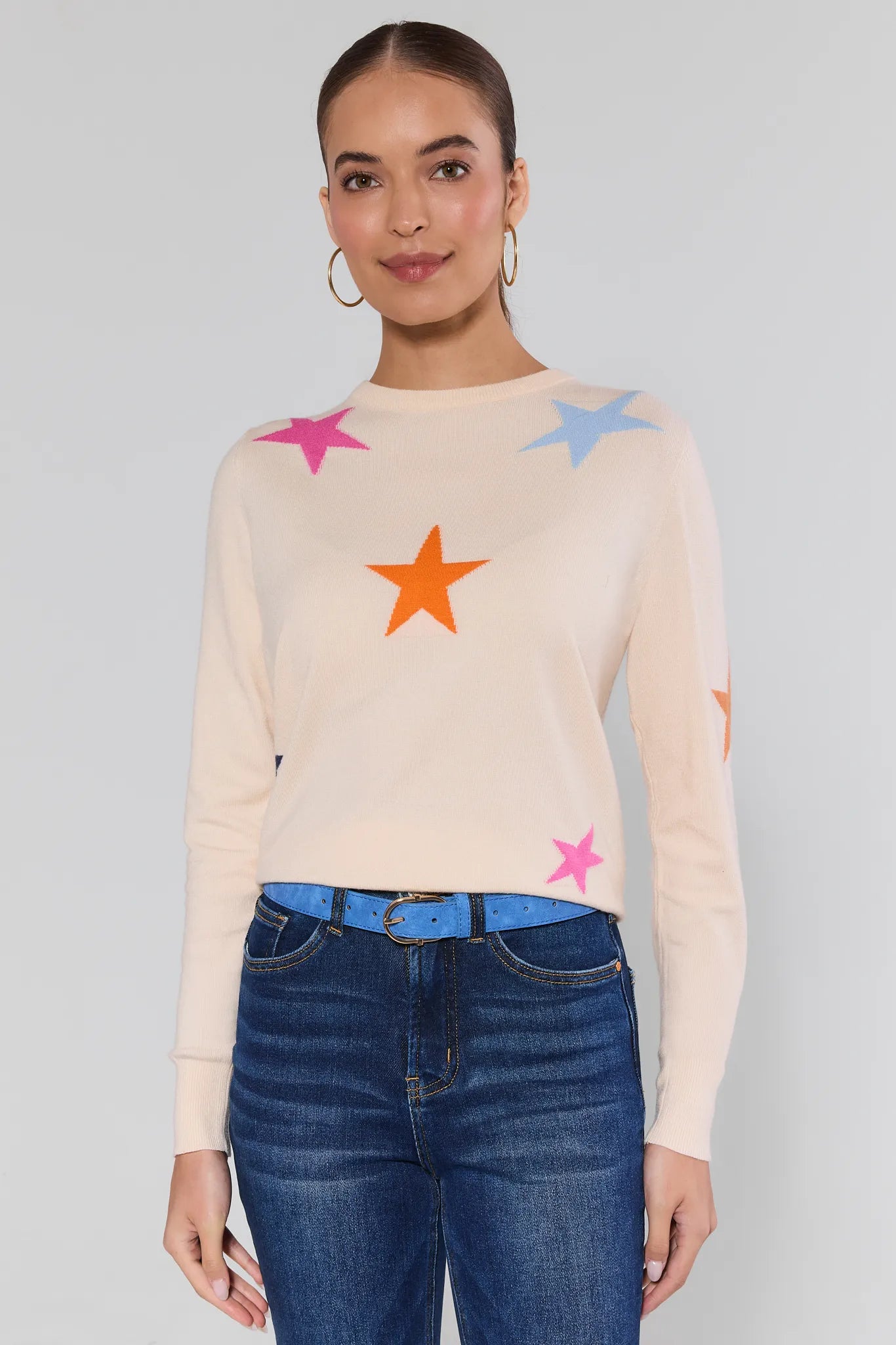 Woman wearing a cream sweater with colorful star patterns and blue jeans on a plain background Luna Cream Star Knit Sweater