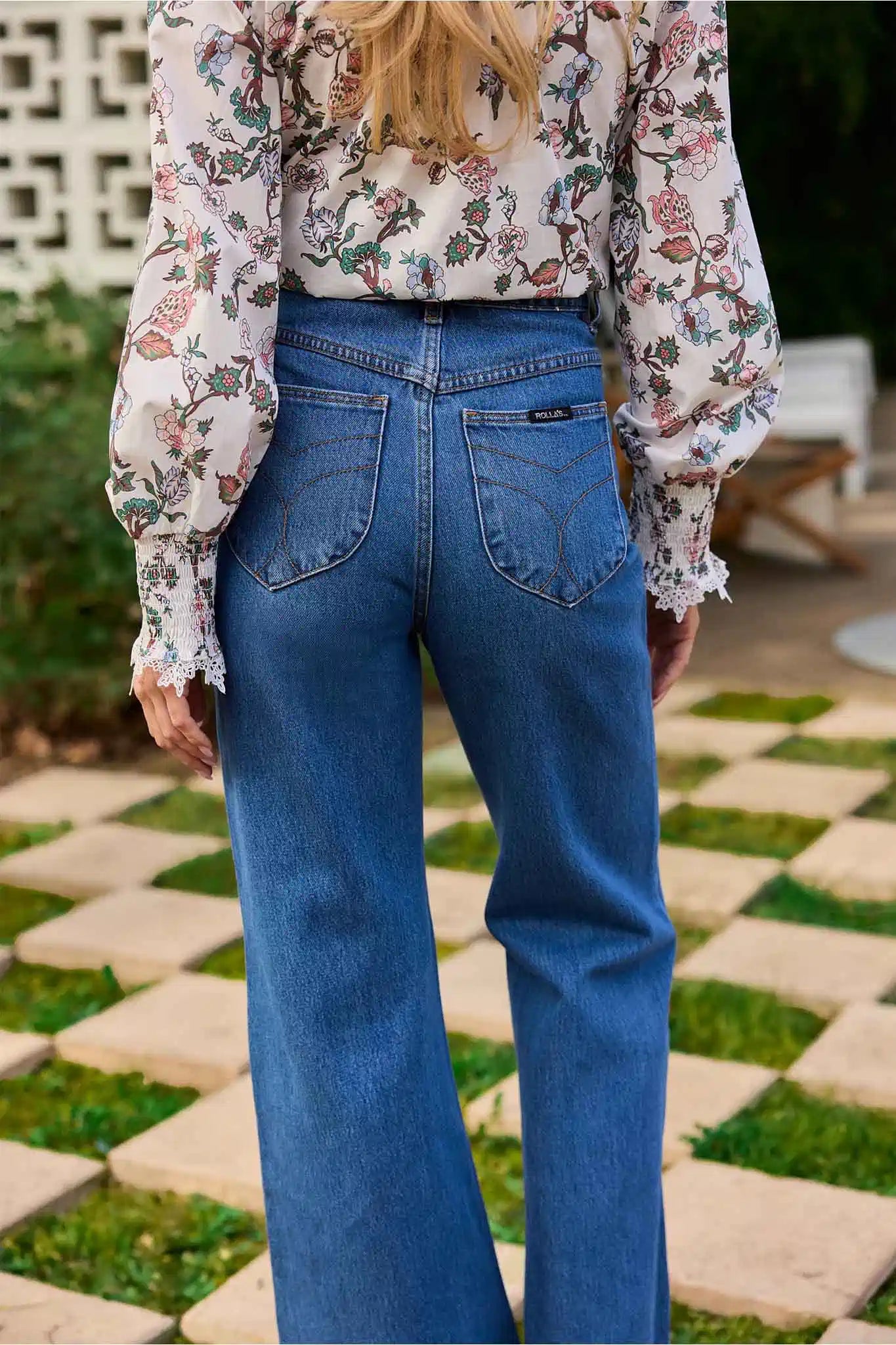 Person wearing a floral blouse and blue jeans standing on a stone patio.