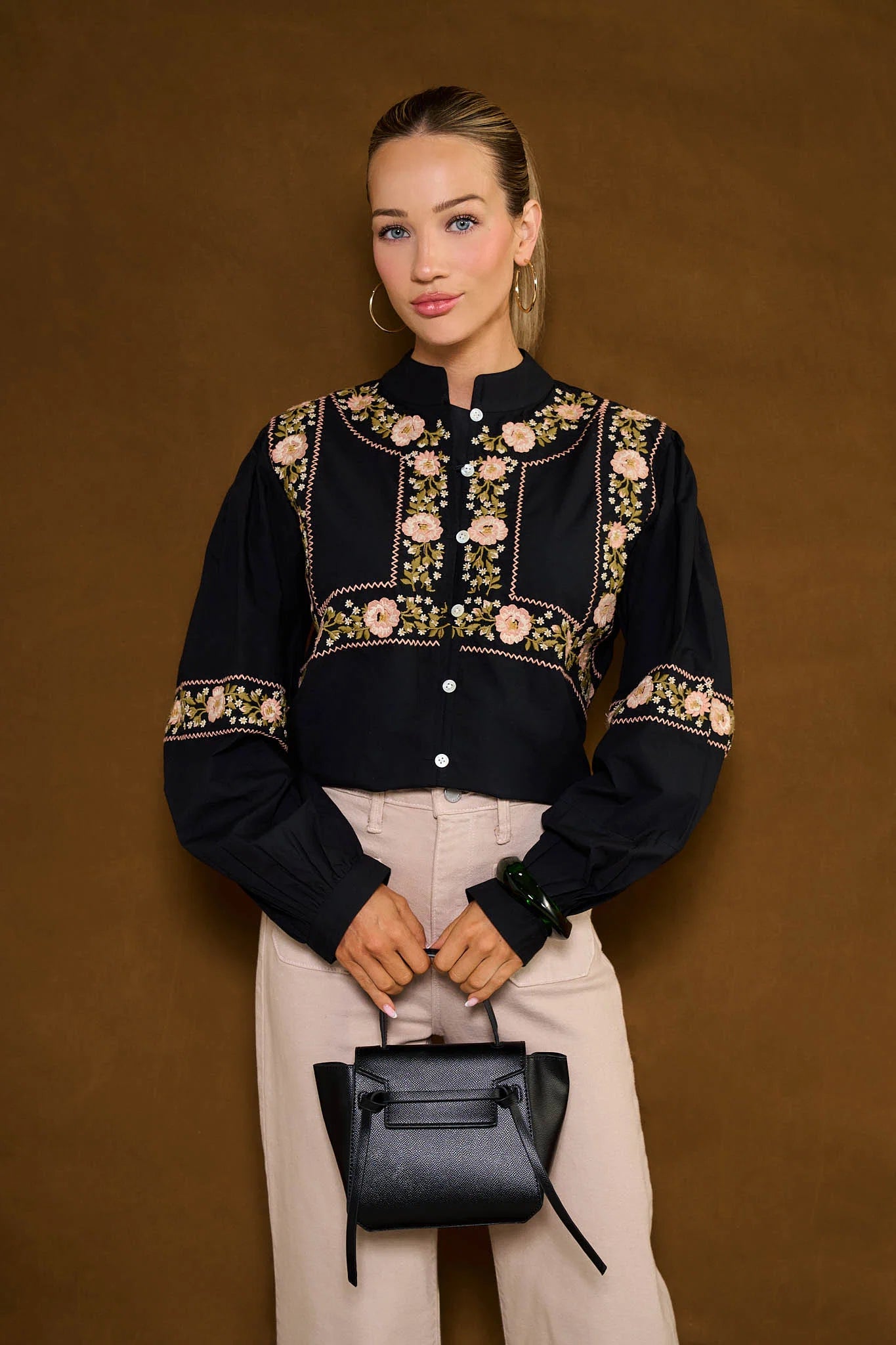 Woman wearing a black embroidered Selma Top with beige pants against a brown background