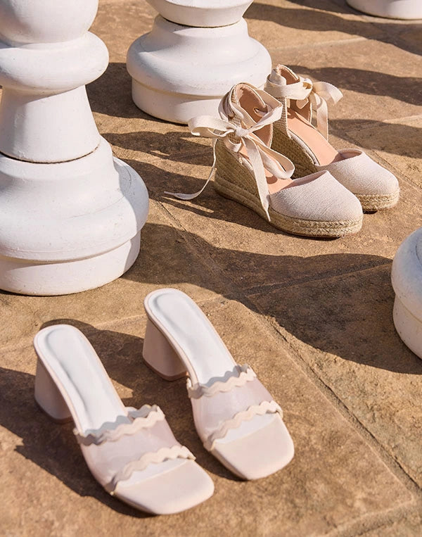 Pair of beige sandals with raffia straps on a sandy surface.