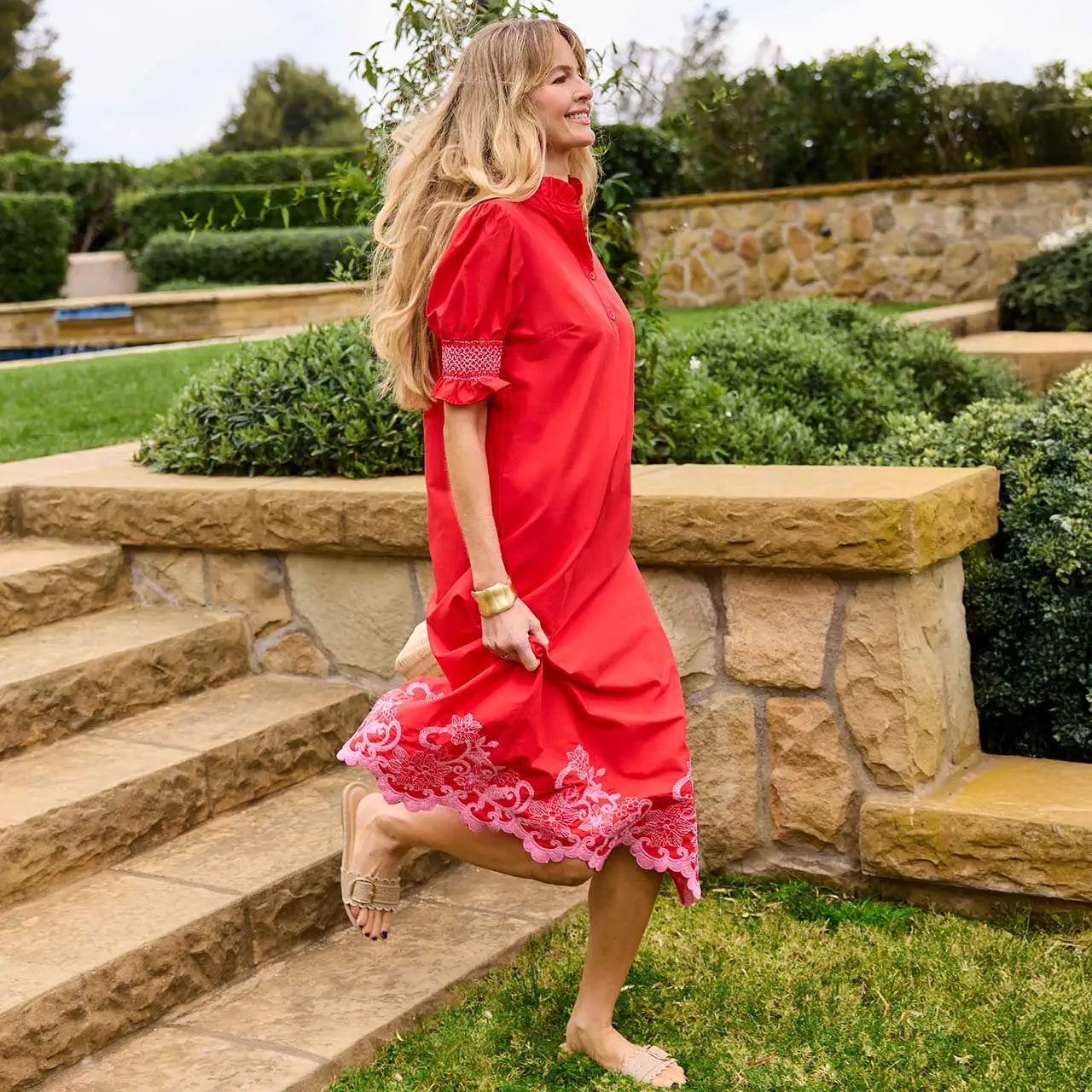 Woman in a red dress standing on stone steps with greenery in the background