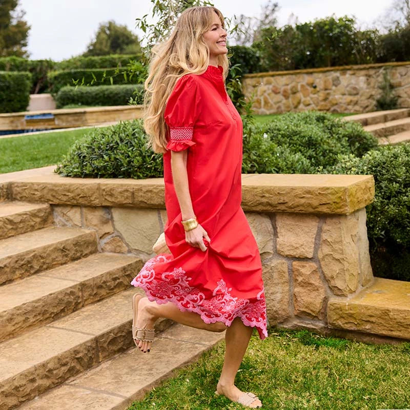 Woman in a red dress standing on stone steps with greenery in the background