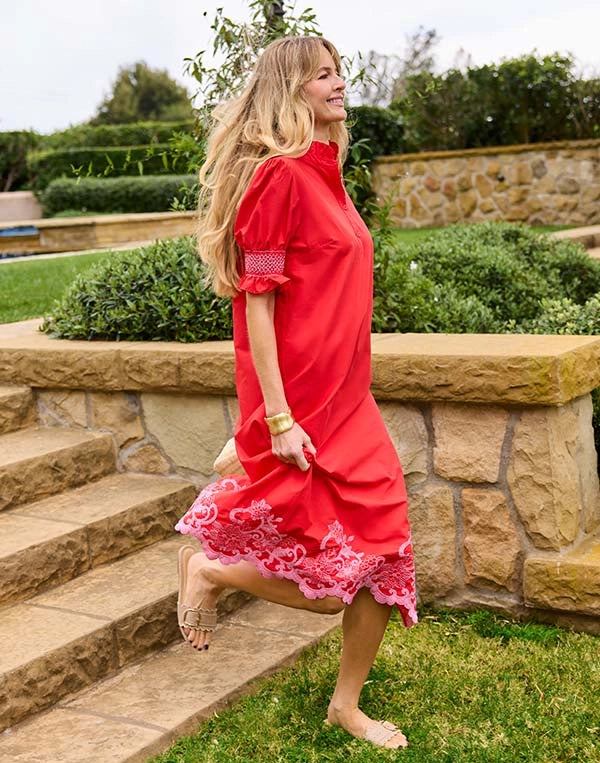 Woman in a red dress standing on stone steps with greenery in the background