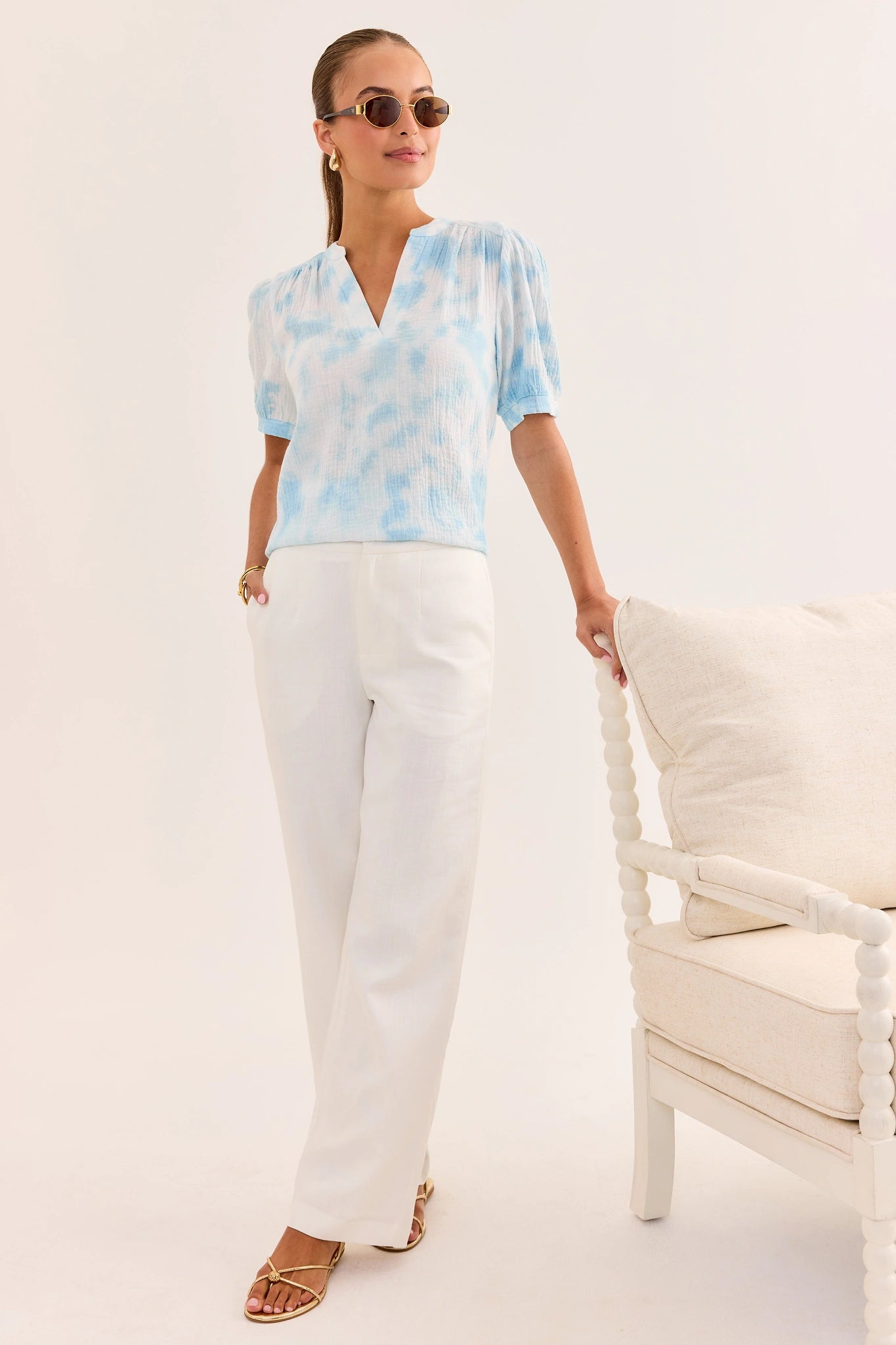 Woman wearing a light blue tie-dye blouse and white pants on a white background lifestyle
