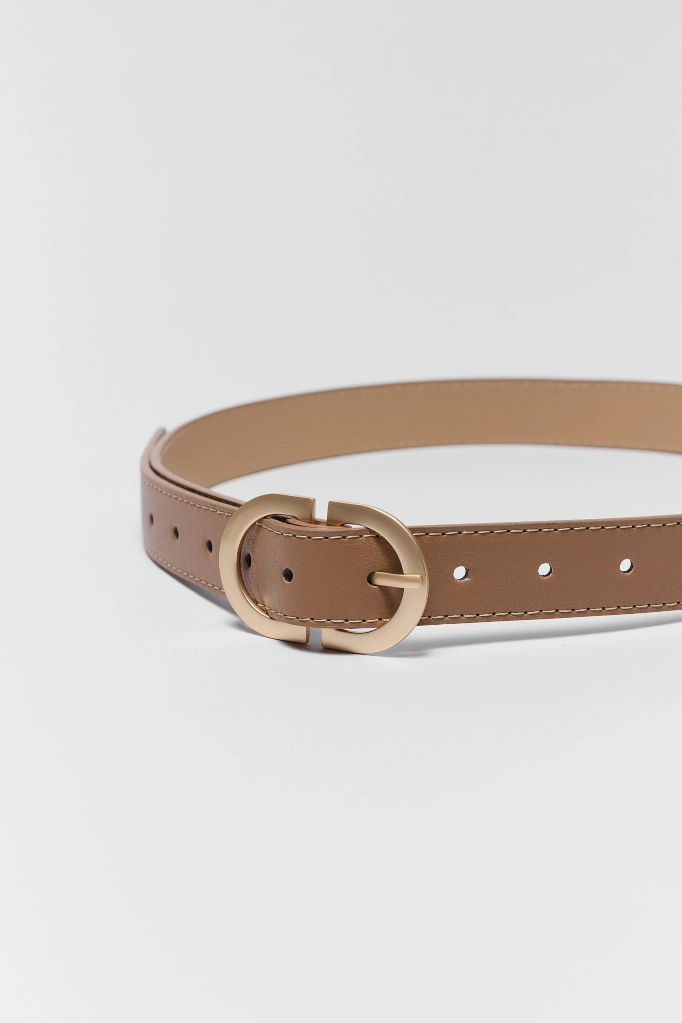 close up Tan leather belt with gold buckle on a light gray background