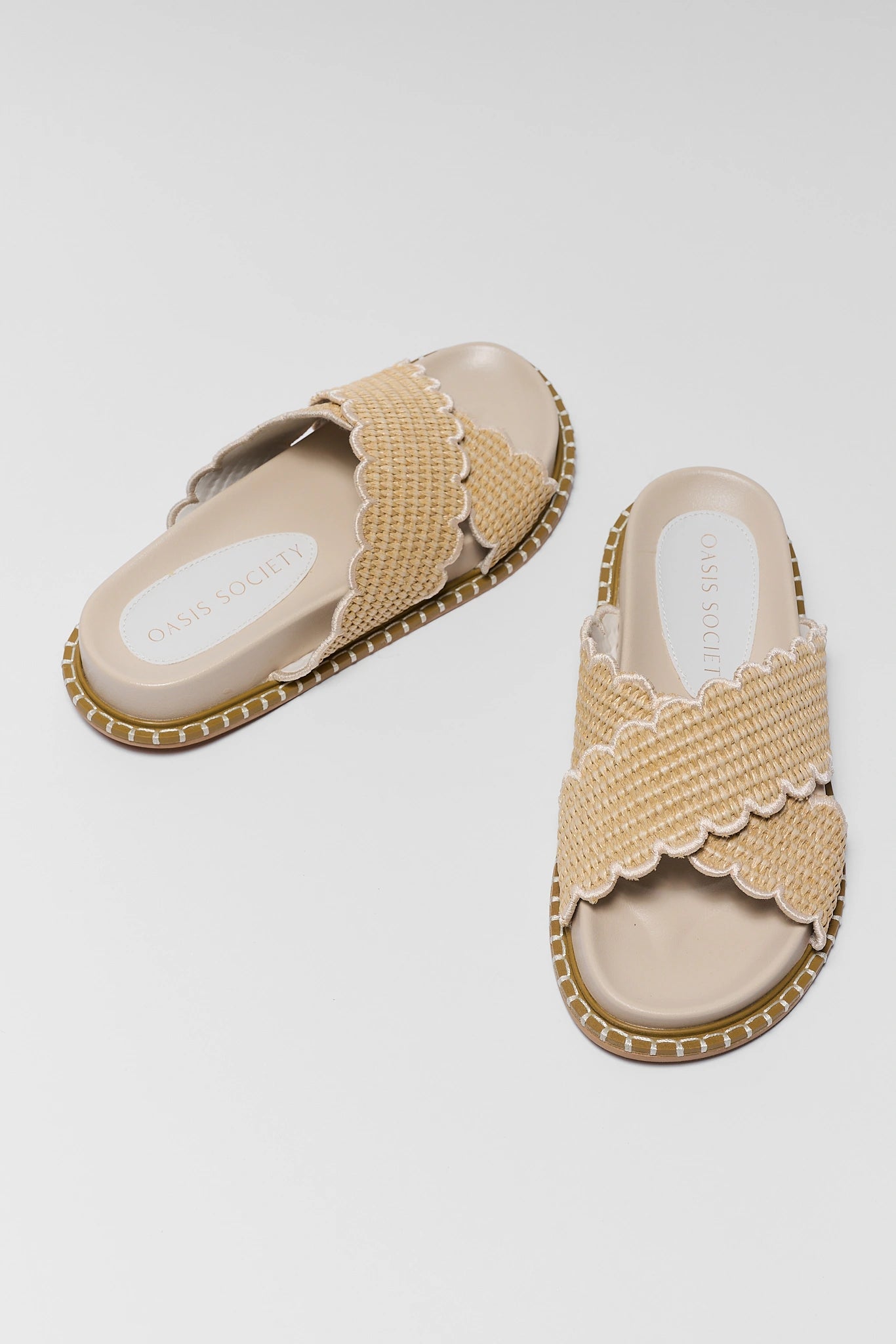 Pair of beige sandals with scalloped edges on a light gray background