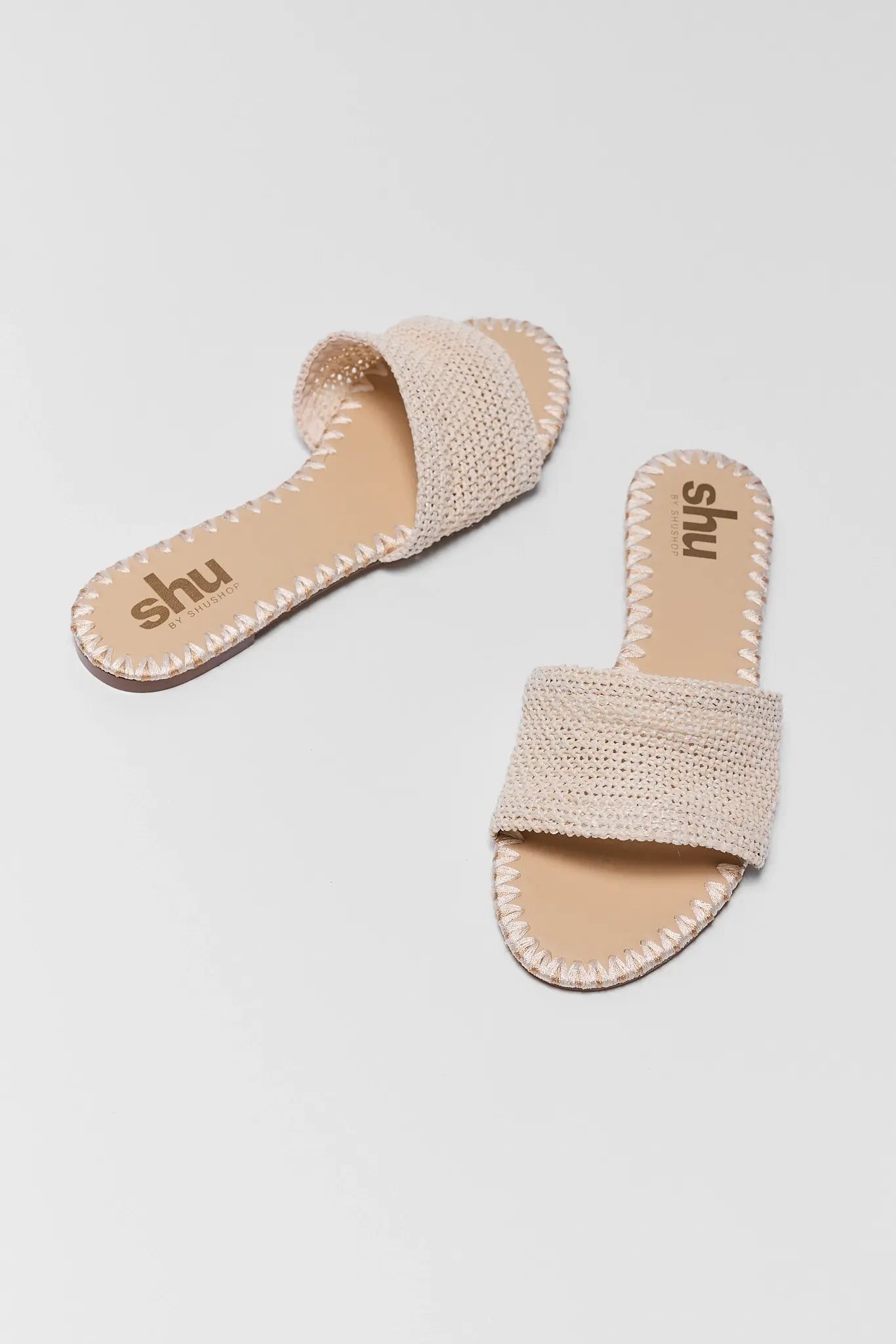Pair of beige sandals with branding on a light gray background