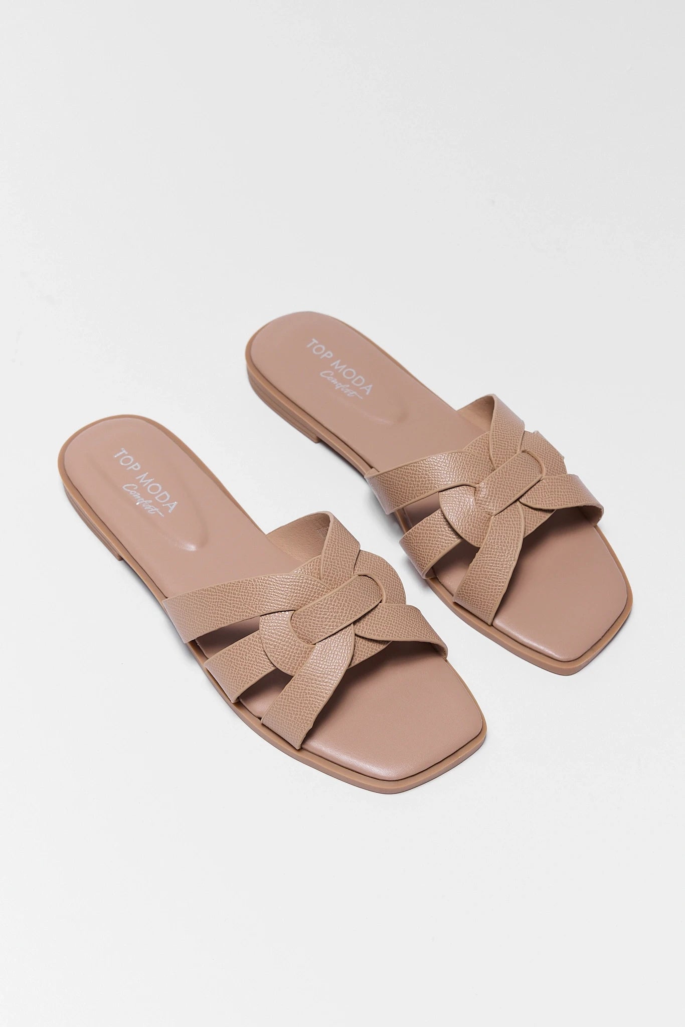 Pair of beige sandals with a knot design on a white background two tan slip on sandals