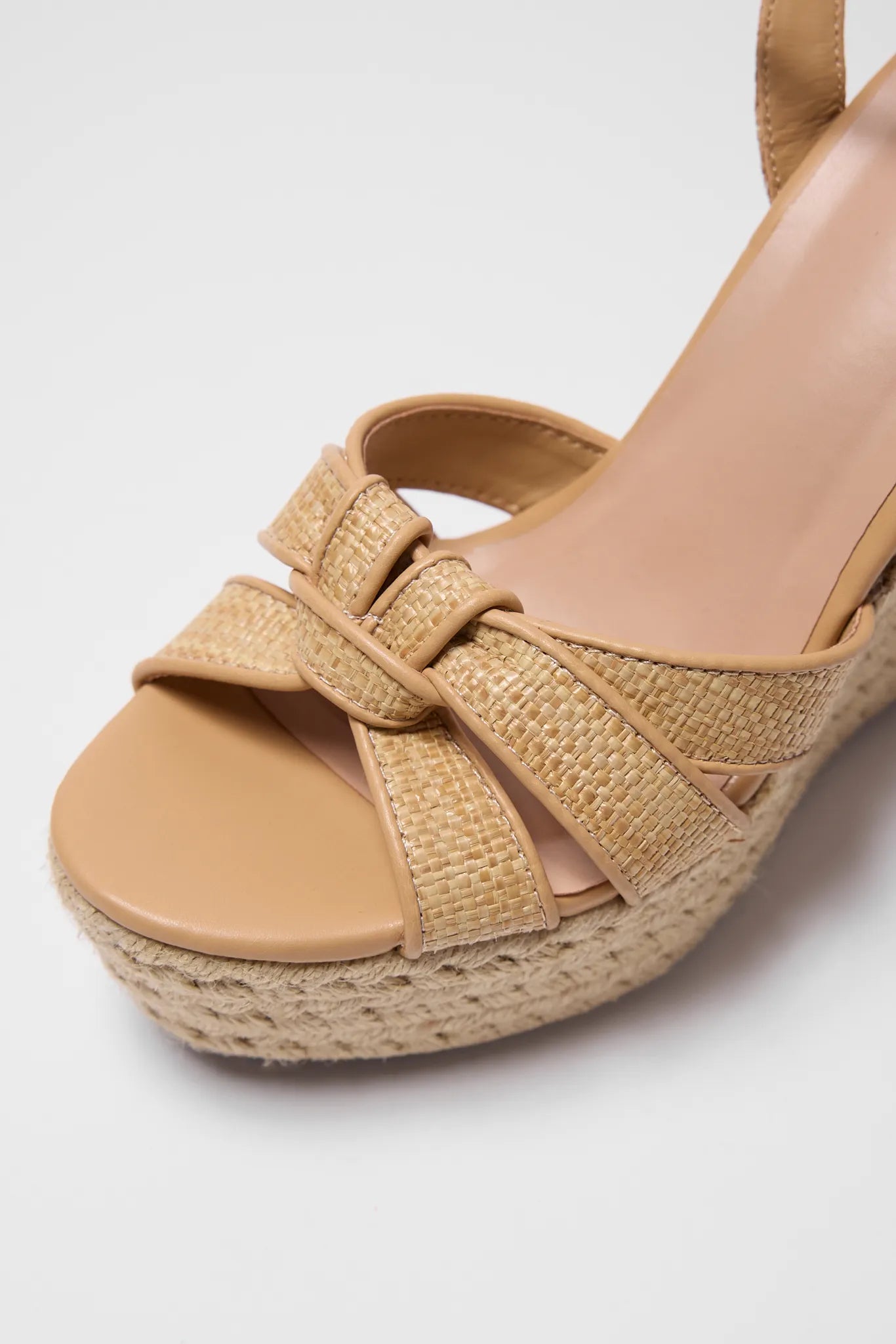 Tan wedge sandal with woven details on a white background