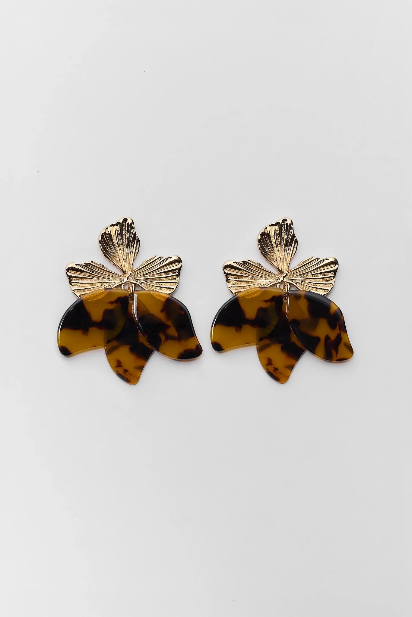 A pair of gold-tone and tortoiseshell acetate flower-shaped earrings on a plain light gray background.