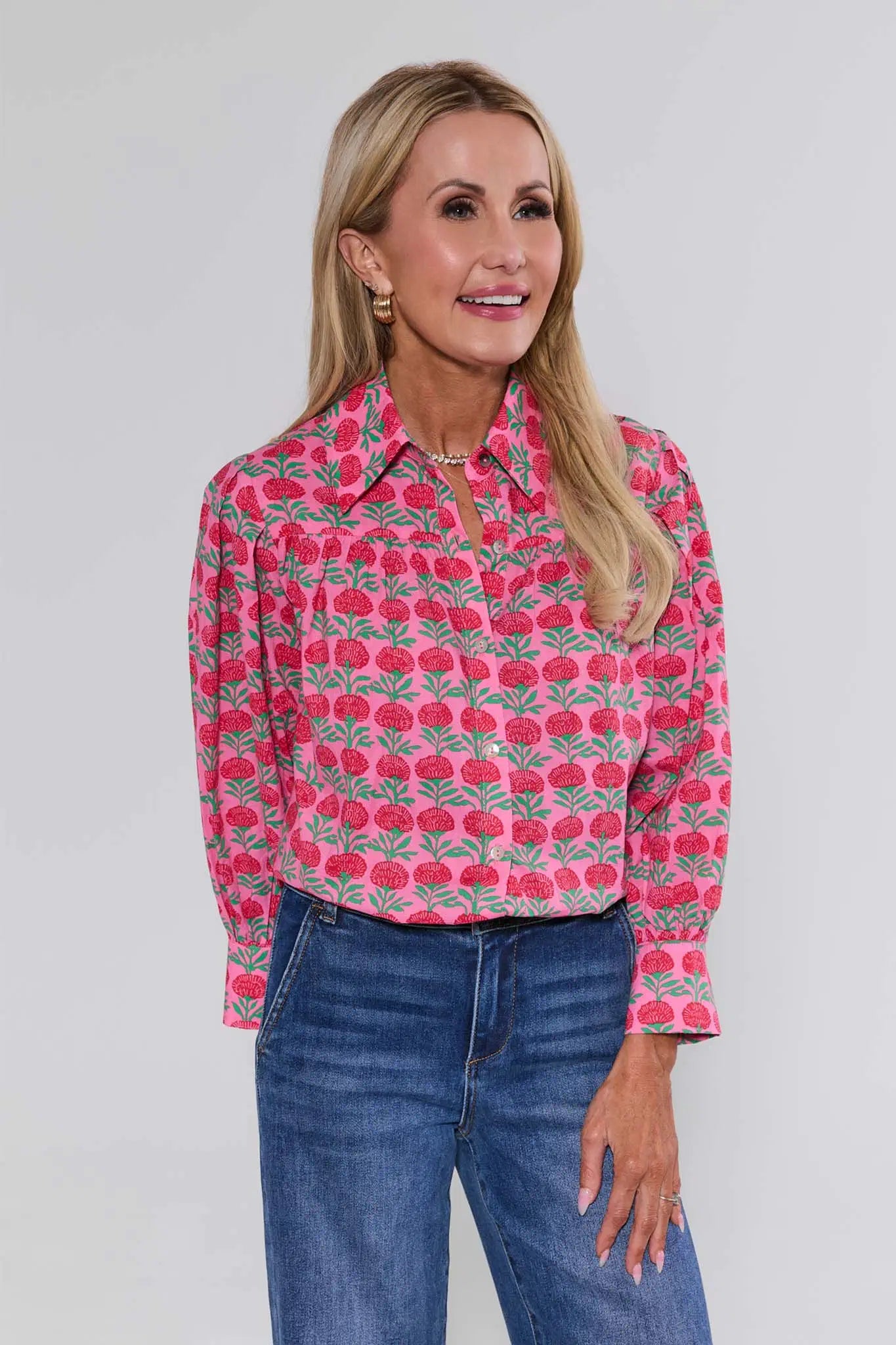 Woman wearing a pink floral patterned shirt and blue jeans against a gray background