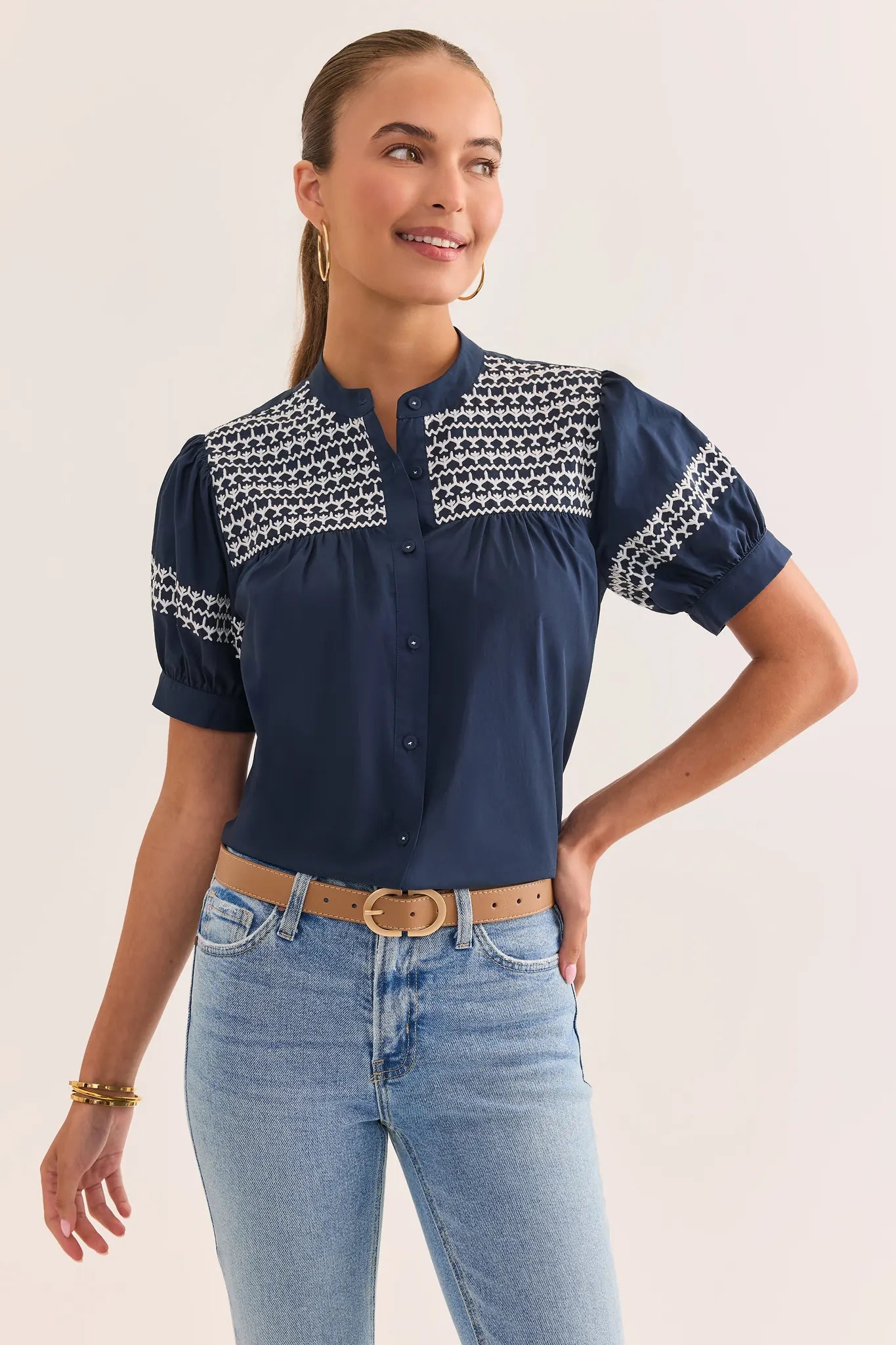 Woman wearing a navy blouse with white patterns and light blue jeans on a plain background lifestyle