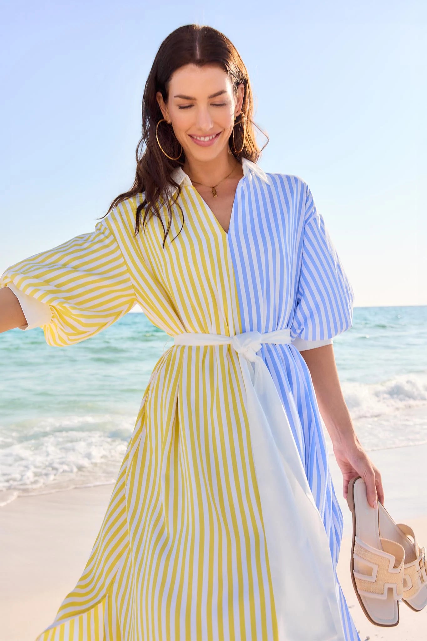 Woman in a yellow and blue striped dress standing on a beach.