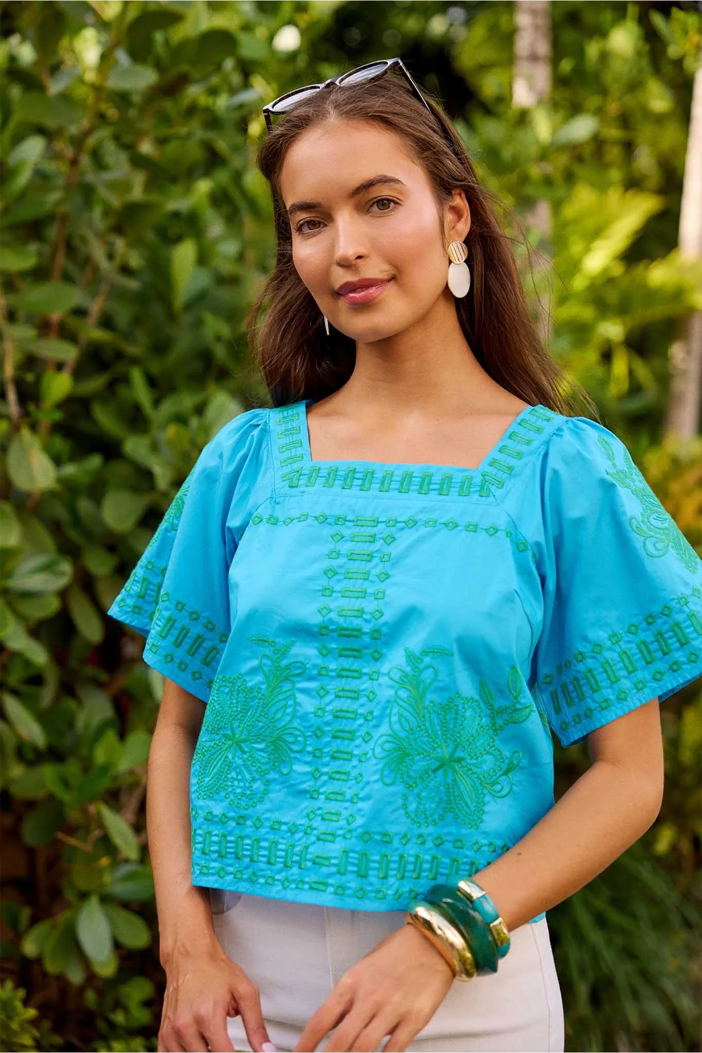 Woman wearing a blue embroidered top with a green leafy background