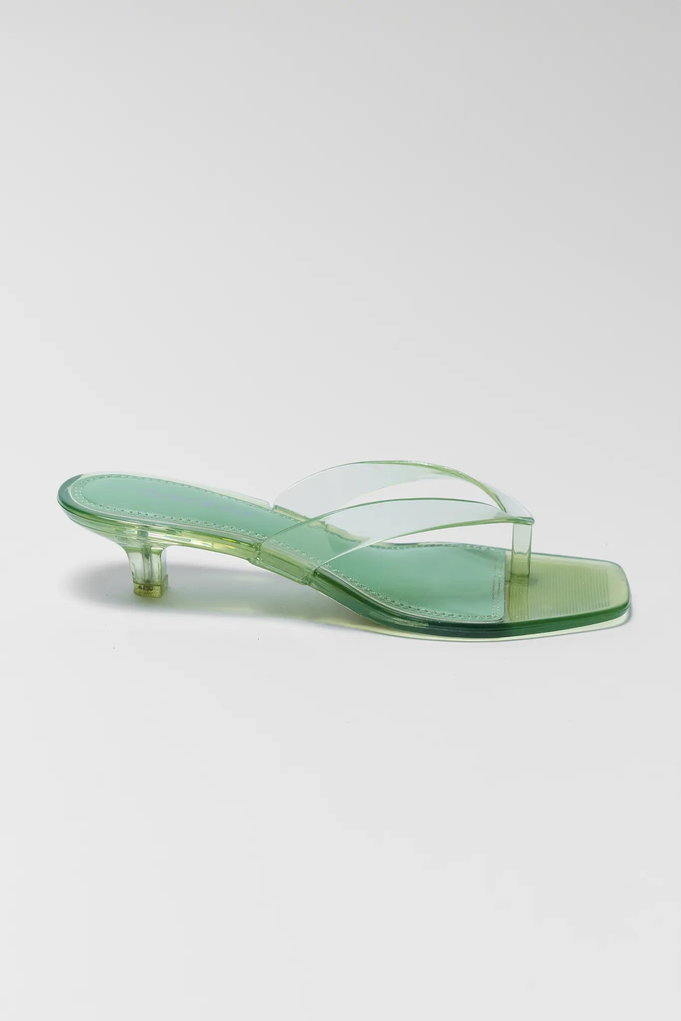 Green sandal with clear heel on a light gray background