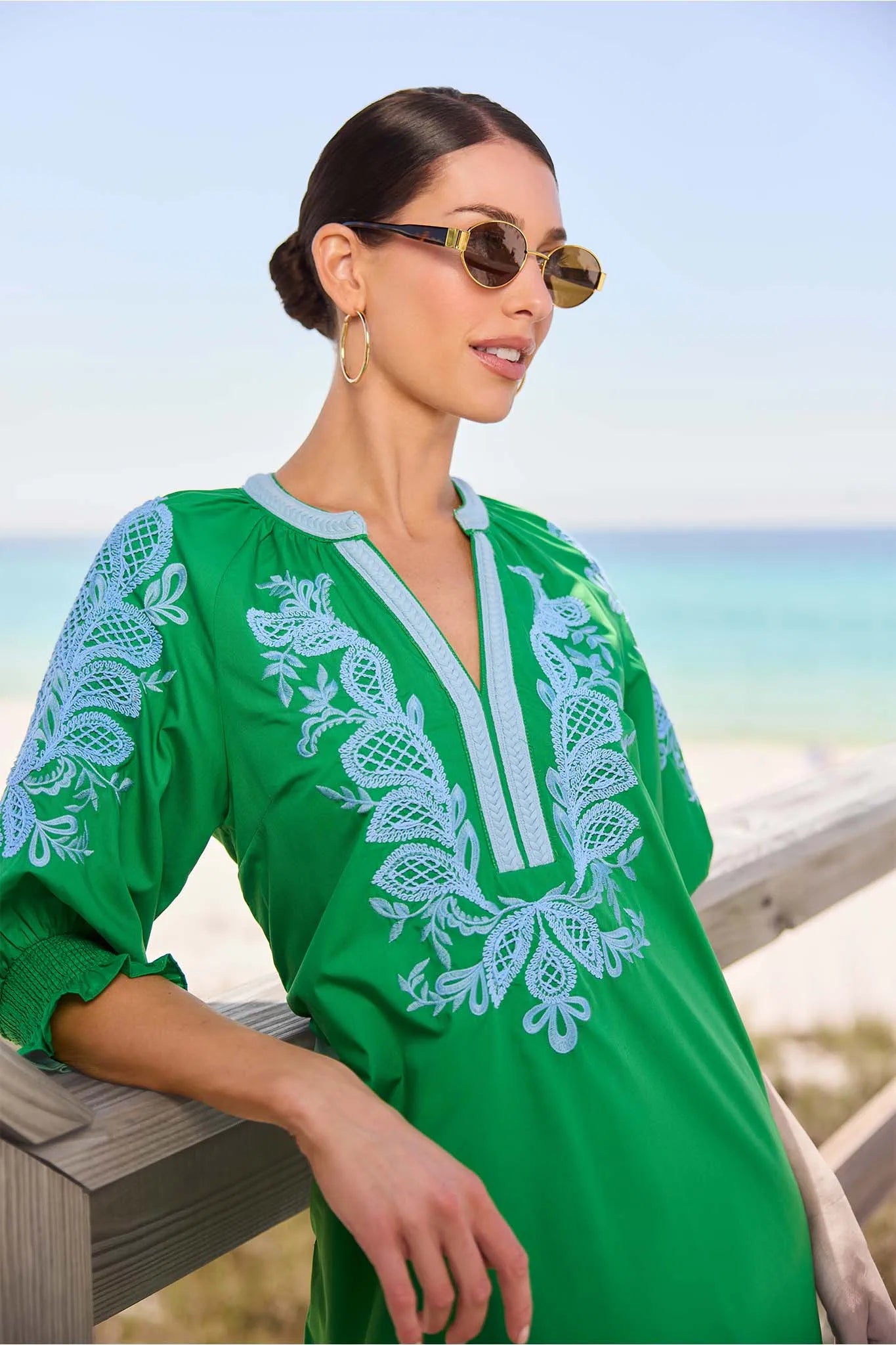 close up Woman wearing a green embroidered dress with sunglasses against a beach background