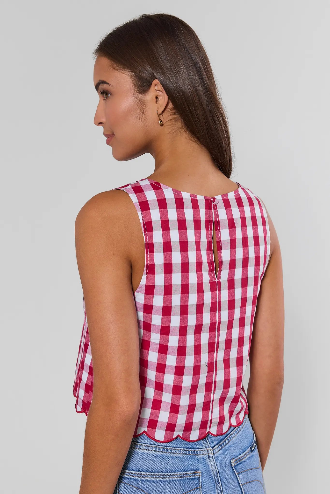 A woman shown from behind wearing a sleeveless red and white gingham check top with a scalloped hem, paired with matching shorts, against a light gray background.
