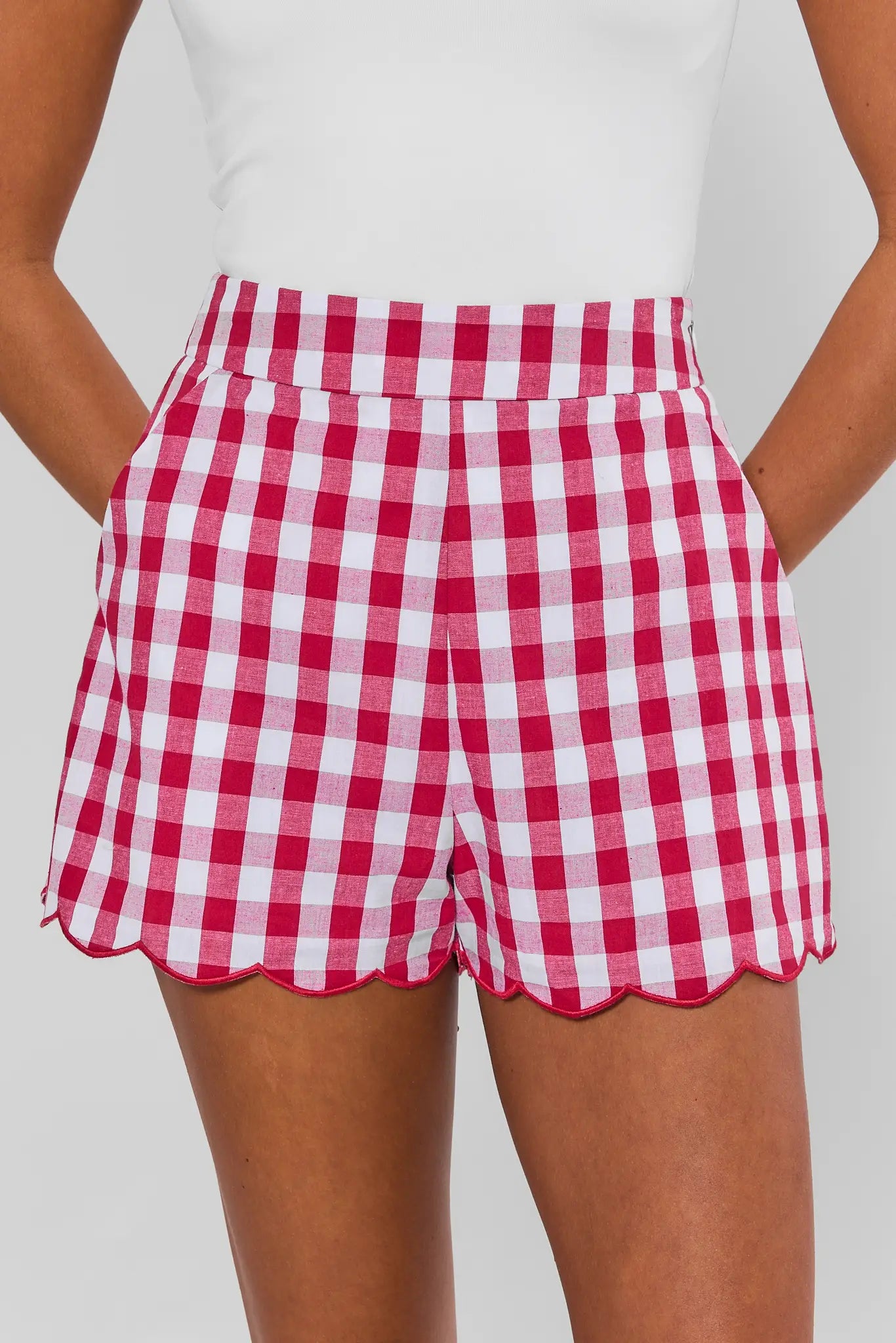 Red and white gingham check patterned shorts with a scalloped hem, shown on a model wearing a white top against a light gray background.