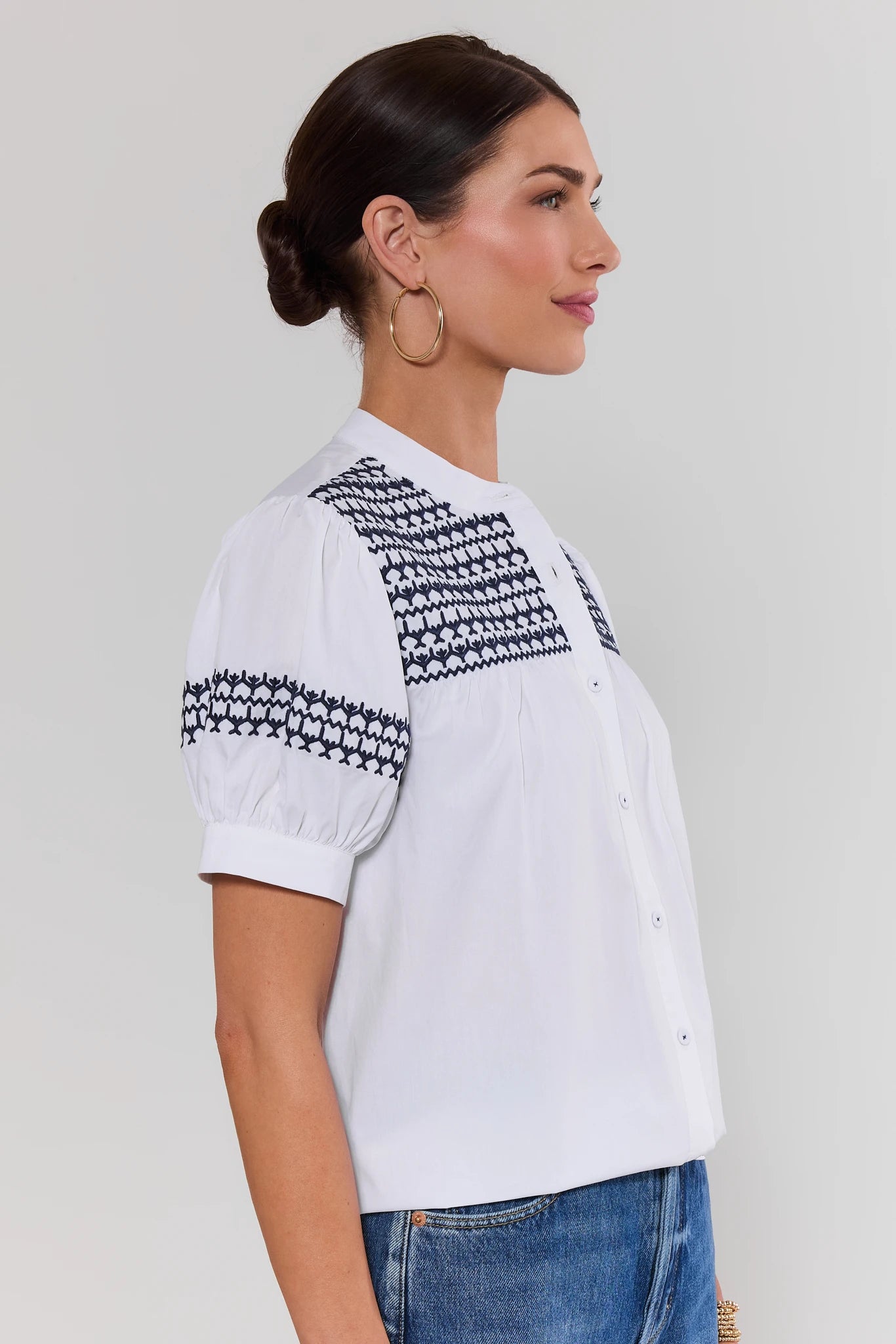 side shot Woman wearing a white blouse with black patterned sleeves on a plain background