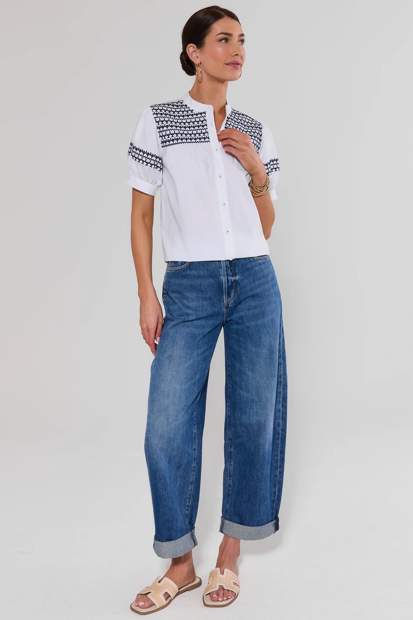 Woman wearing a white blouse with navy patterns and blue jeans on a light gray background