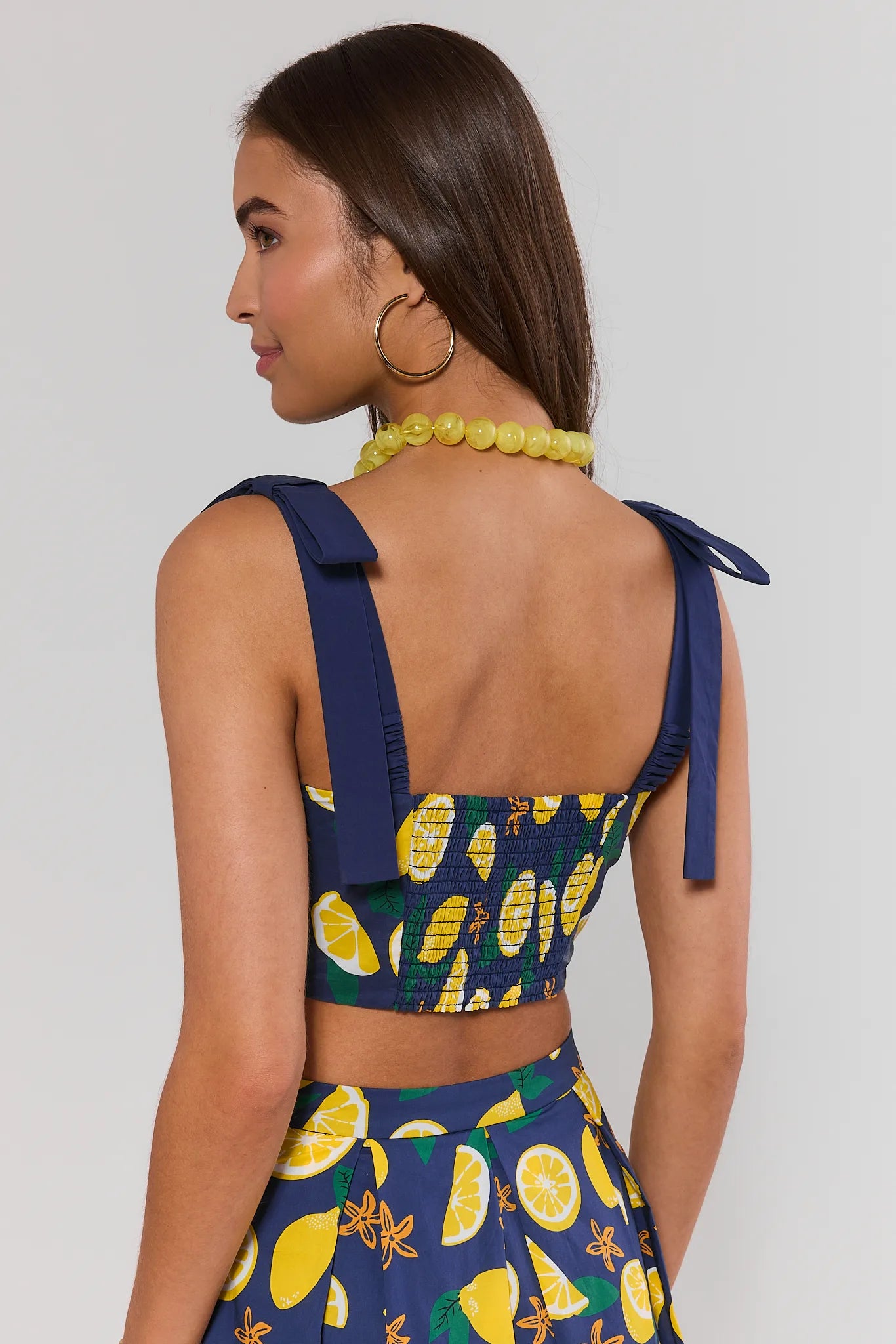 Woman standing wearing a blue and yellow patterned outfit with lemon design on a plain background