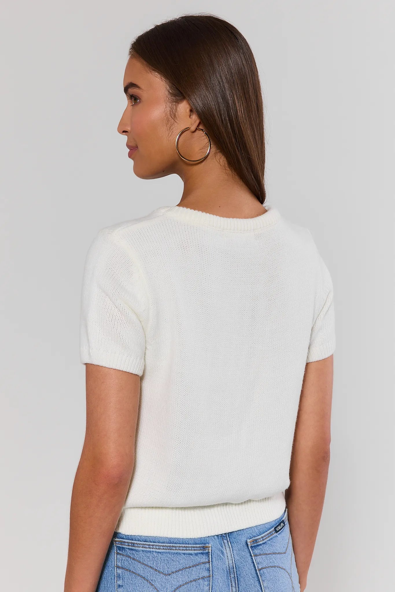 Woman standing wearing a white t-shirt and blue jeans against a plain background