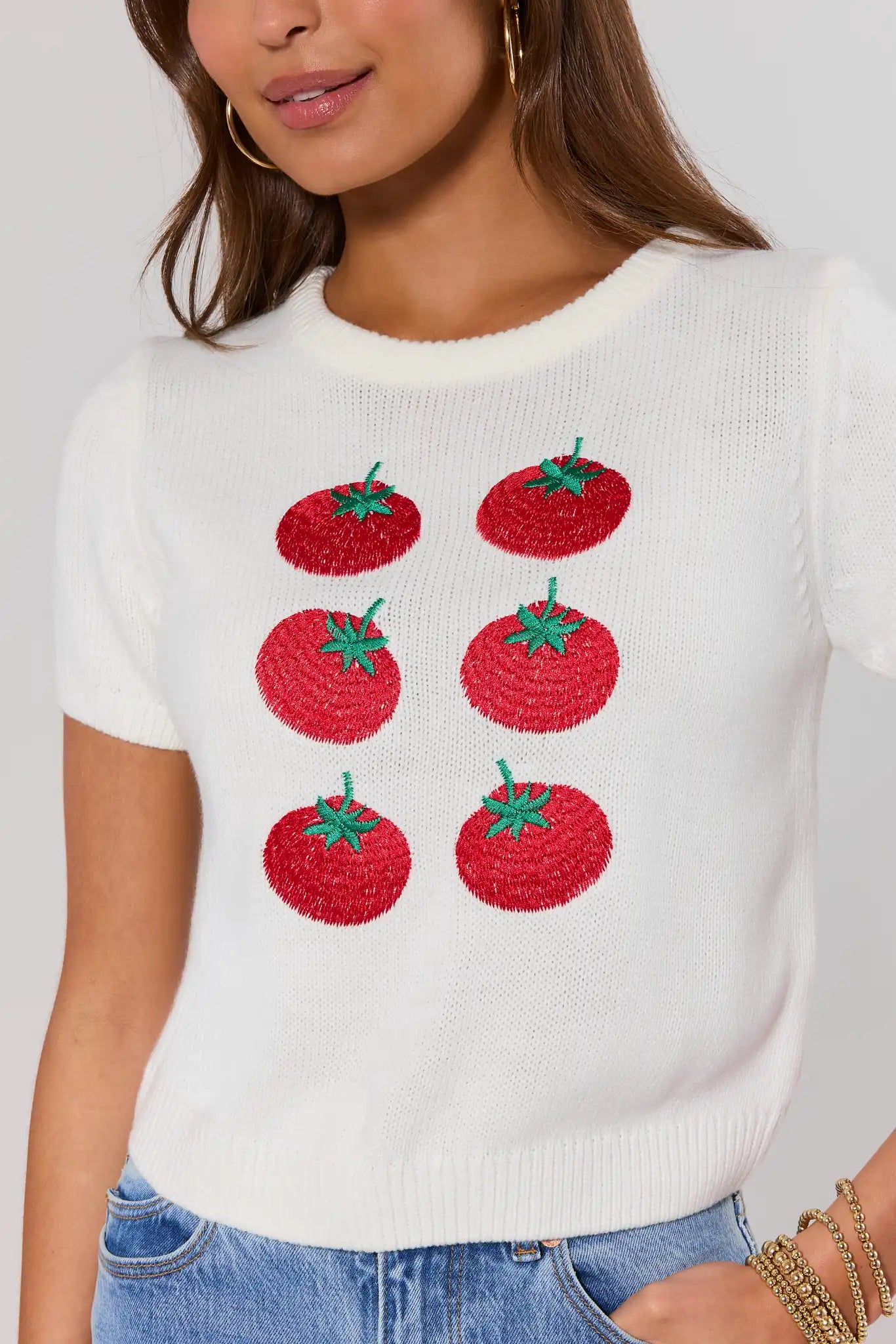 close up mWhite sweater with red tomato designs worn by a person on a plain background