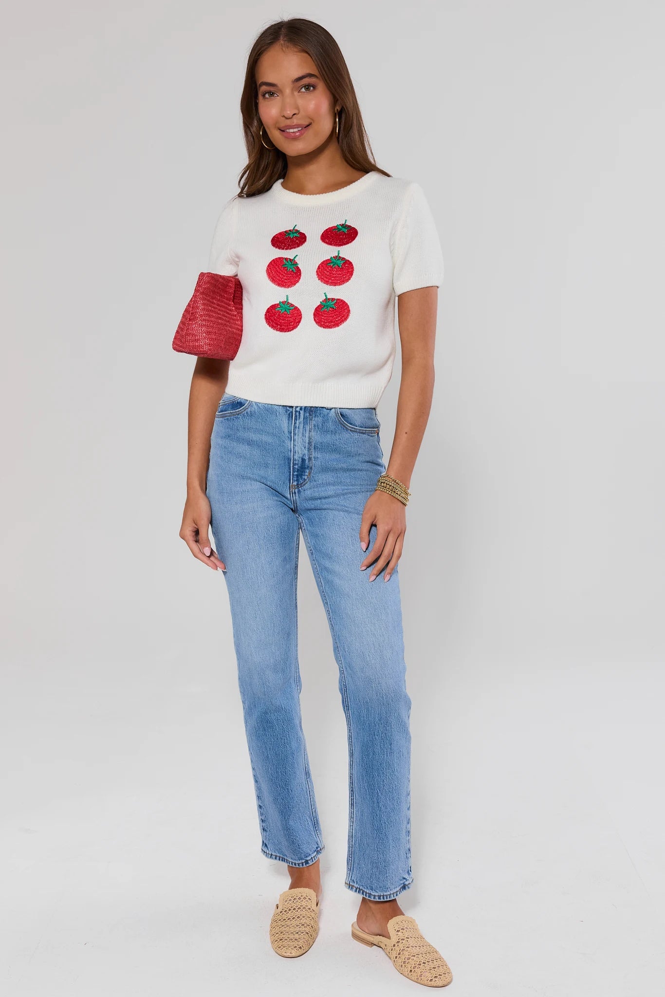 Woman wearing a white t-shirt with red tomato designs and blue jeans on a plain background