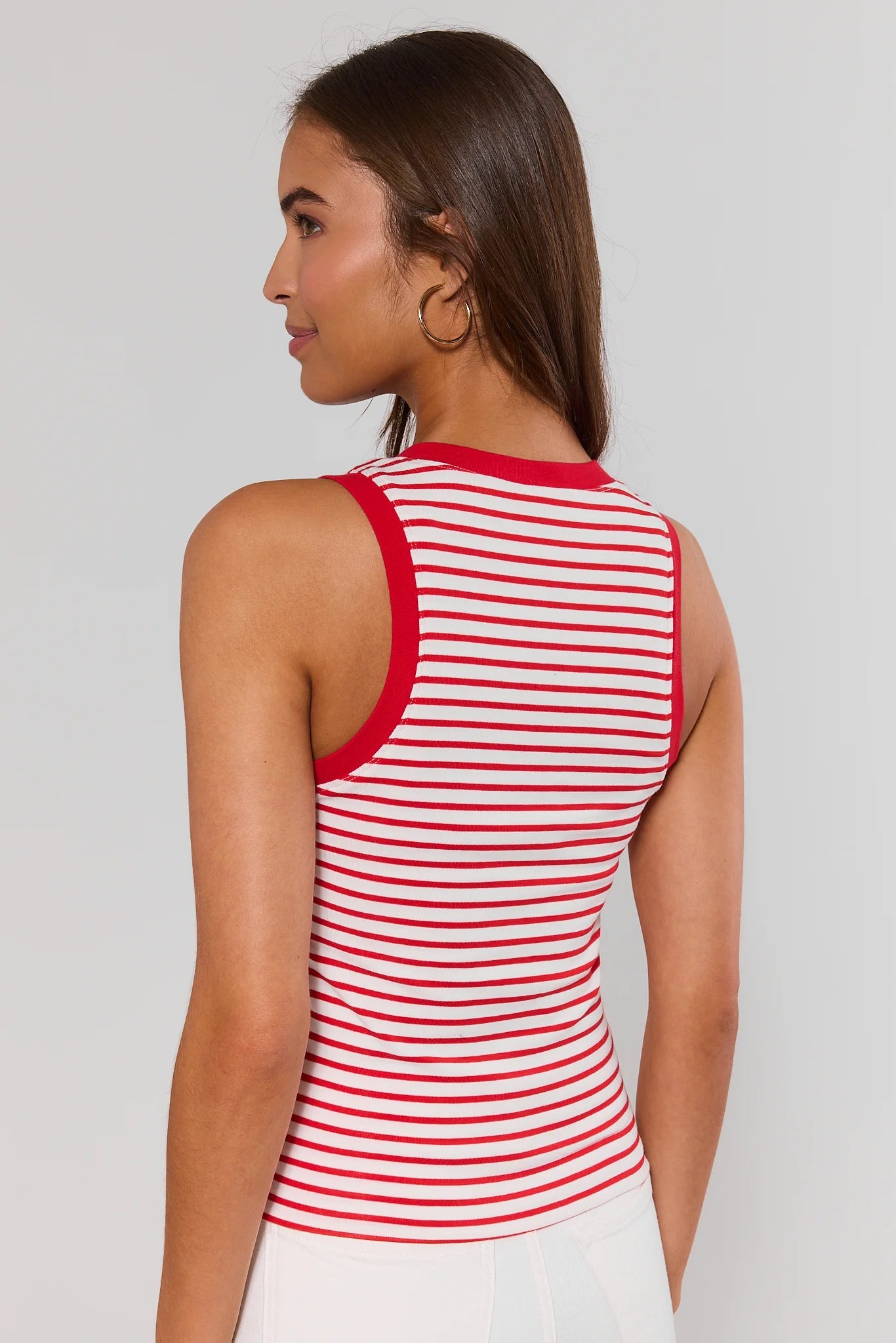 Woman standing wearing a red and white striped sleeveless top against a plain background