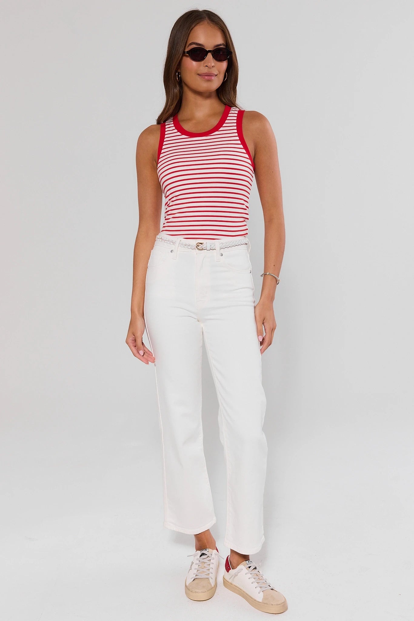 Woman wearing a red and white striped tank top and white pants on a plain background