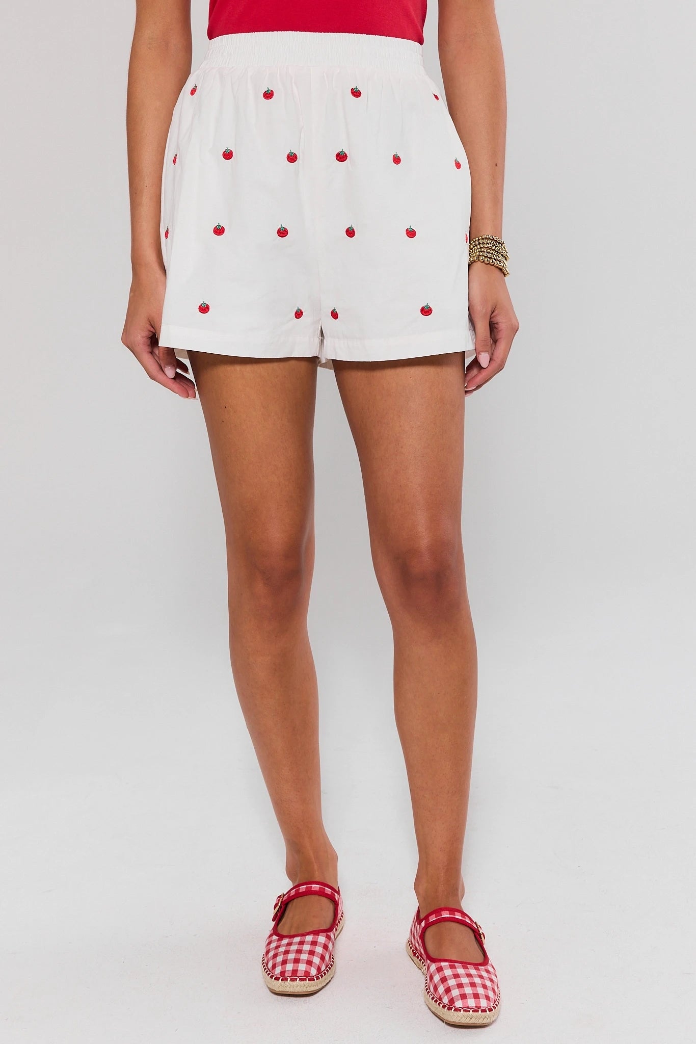 Person wearing white shorts with red polka dots and red checkered shoes on a plain background