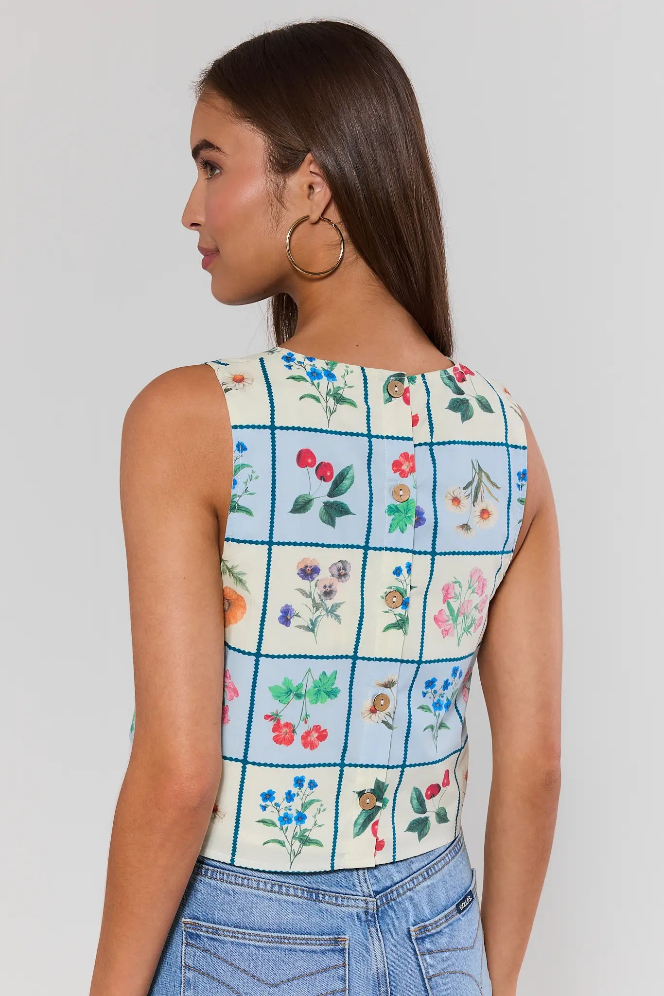 Woman standing wearing a sleeveless top with floral pattern on a plain background