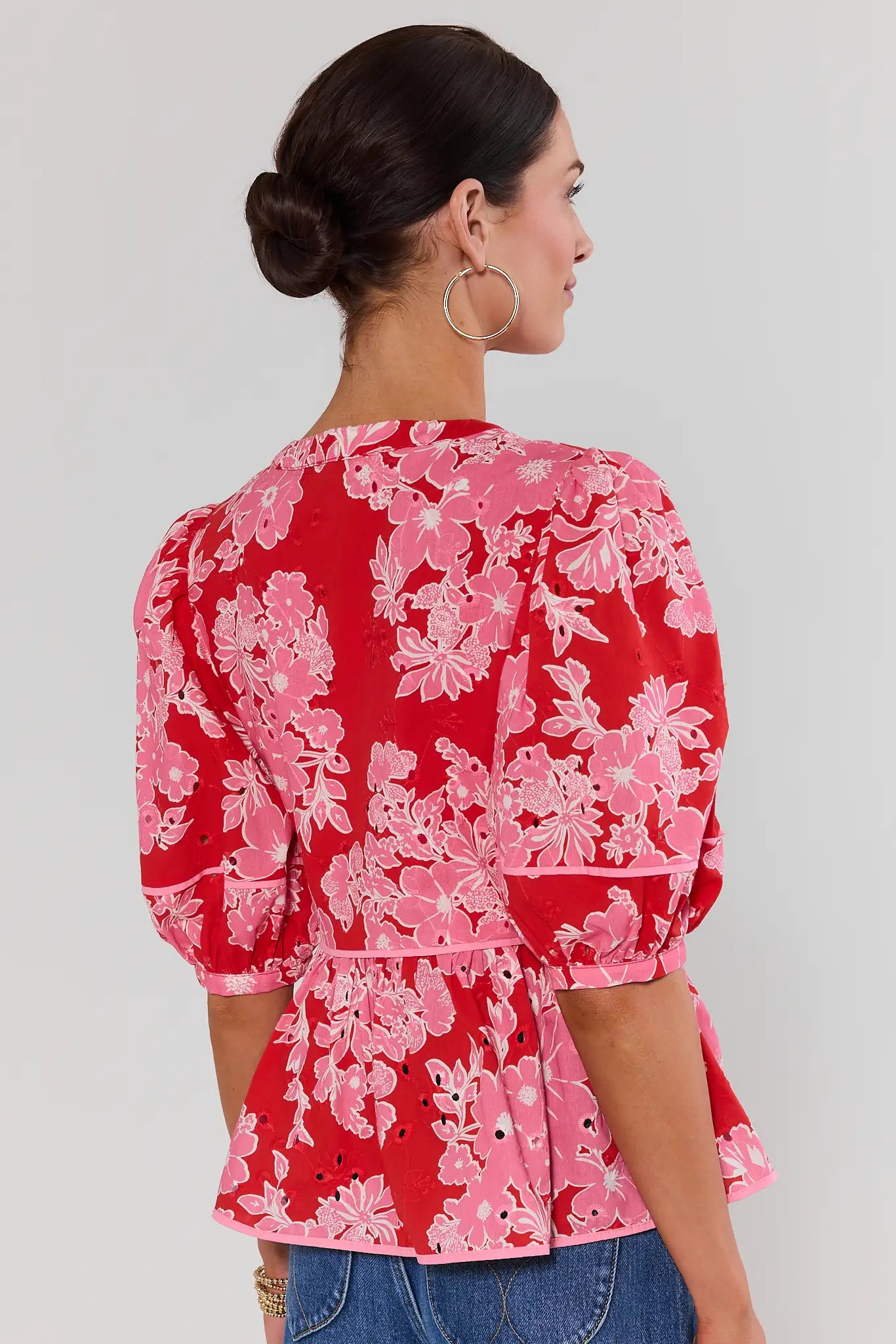 Woman standing wearing a red floral blouse against a white background