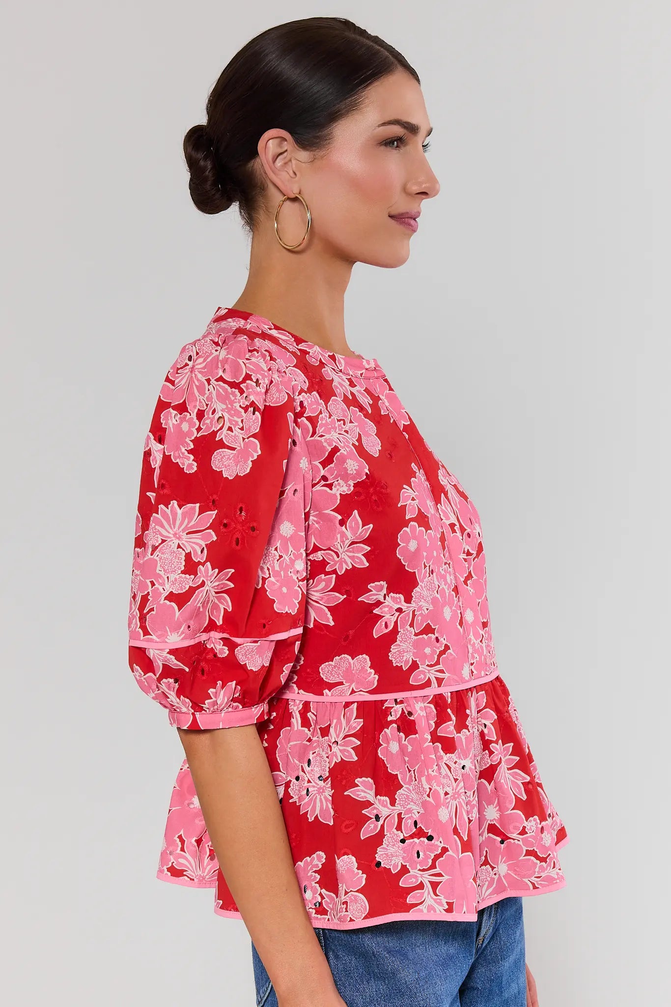 side shot Woman wearing a red floral blouse against a plain background
