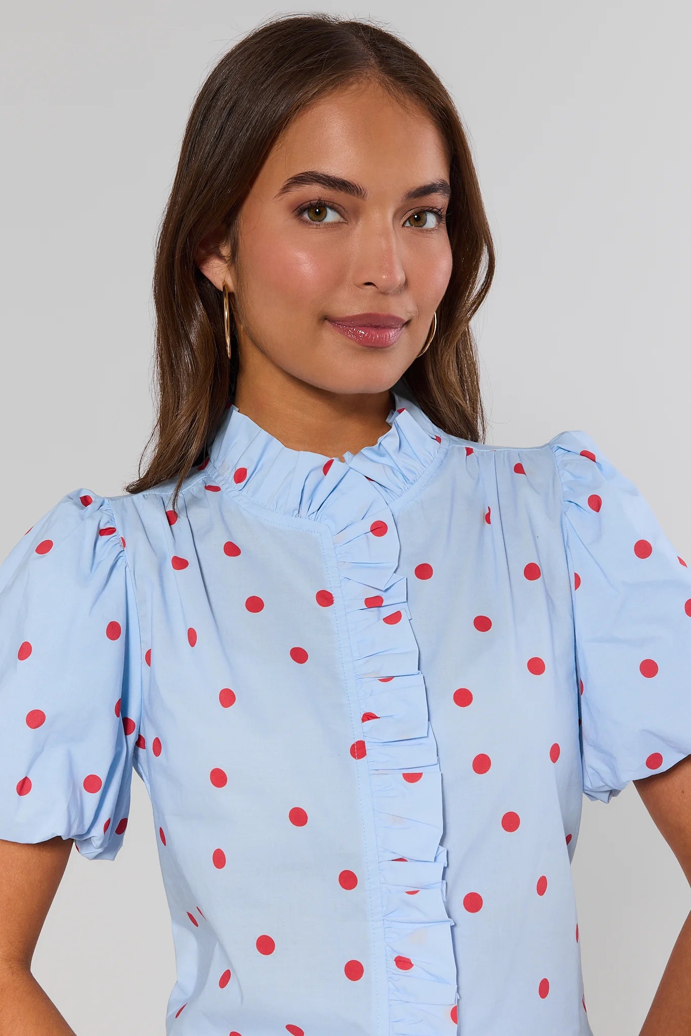 close up Woman wearing a light blue blouse with red polka dots against a plain background