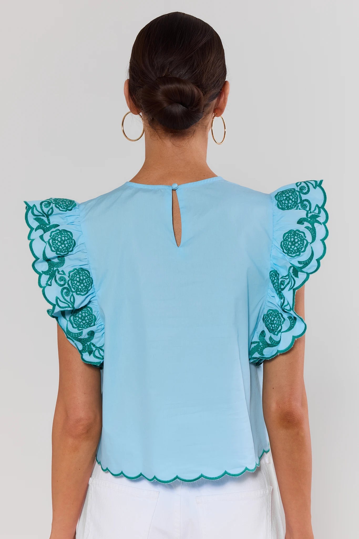 Light blue blouse with green floral embroidery on sleeves and hem, worn by a person against a plain background.