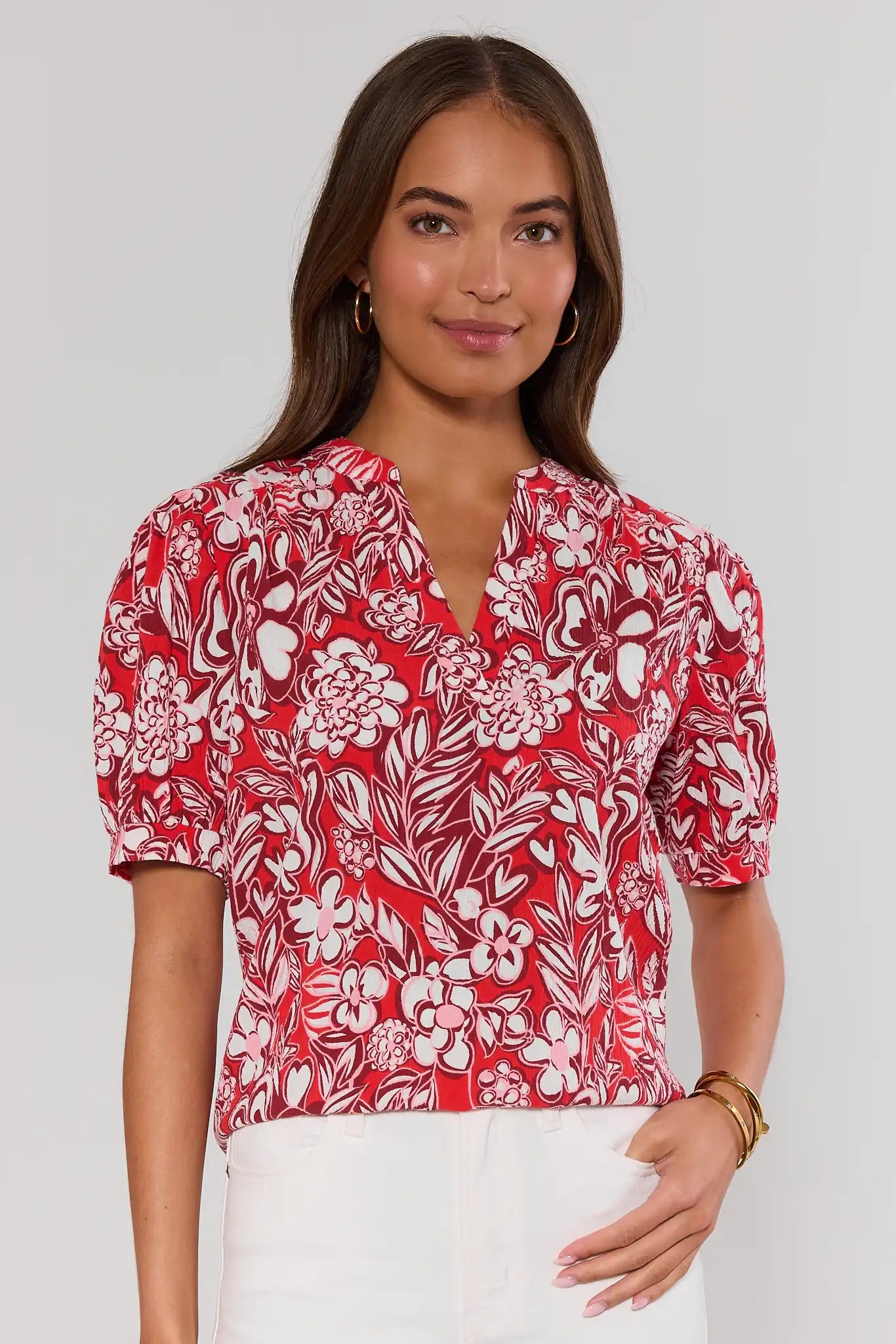 Woman standing wearing a red floral blouse against a white background