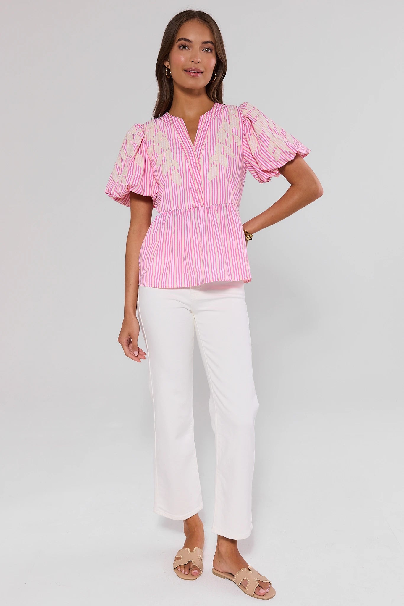 Woman wearing a pink and white striped blouse with ruffled sleeves on a gray background