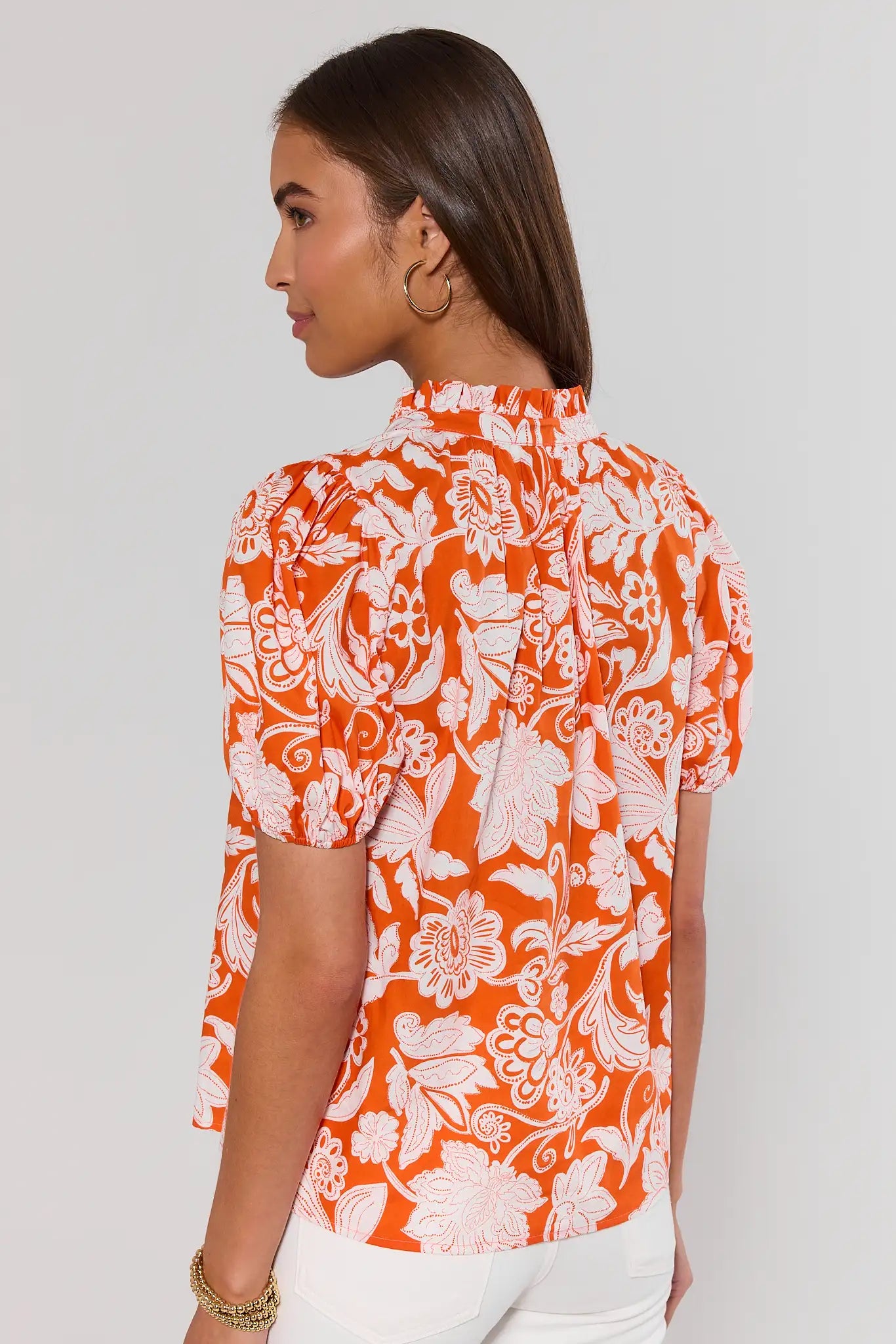 Woman standing wearing an orange and white floral blouse against a plain background