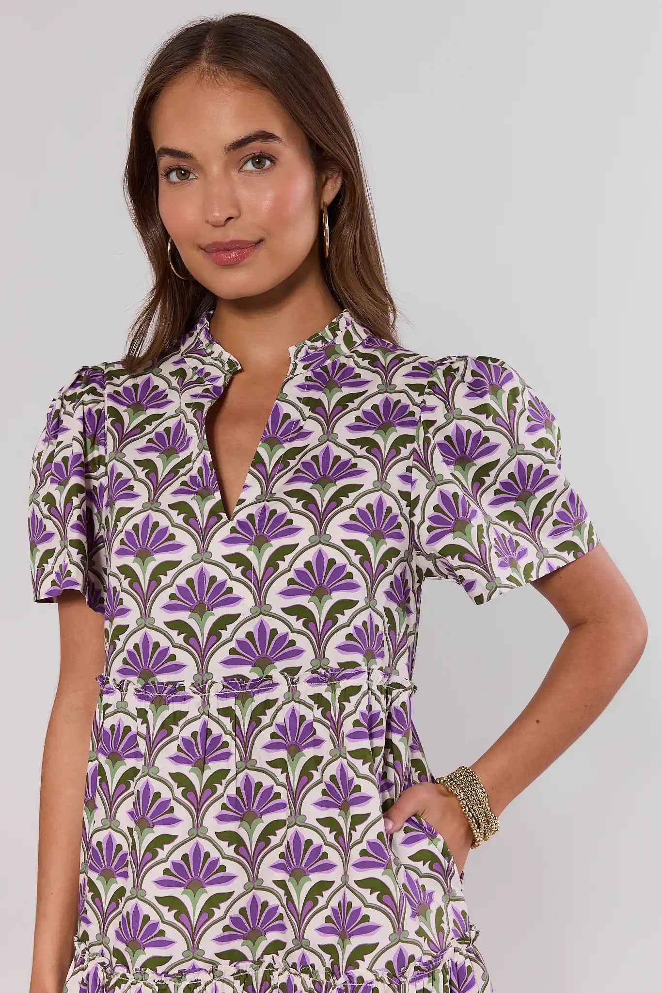 close up Woman wearing a patterned dress with purple and green design on a plain background