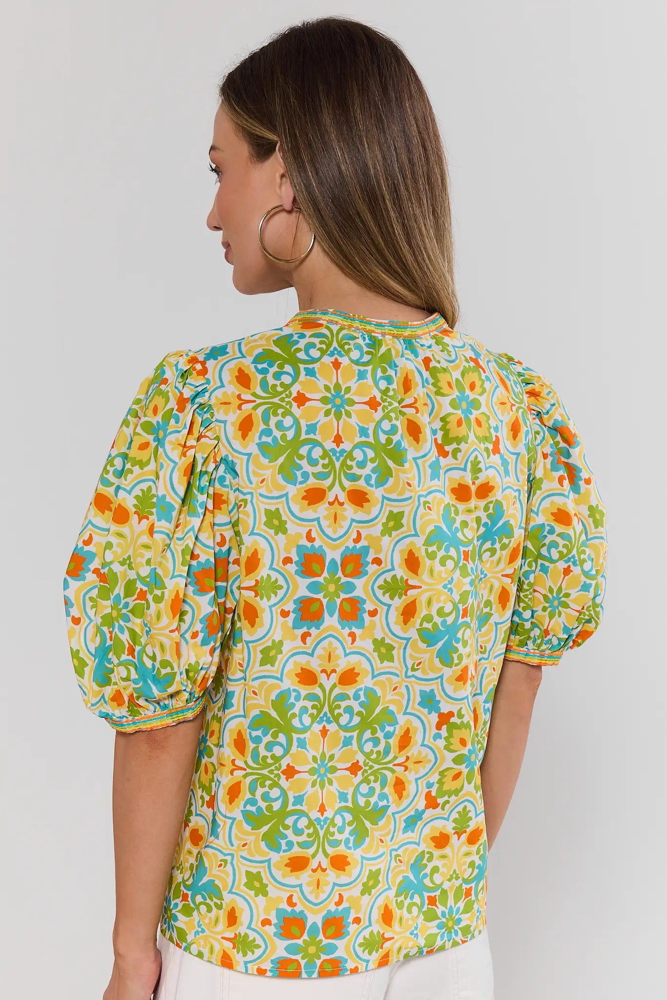Woman wearing a colorful floral patterned blouse against a plain background standing