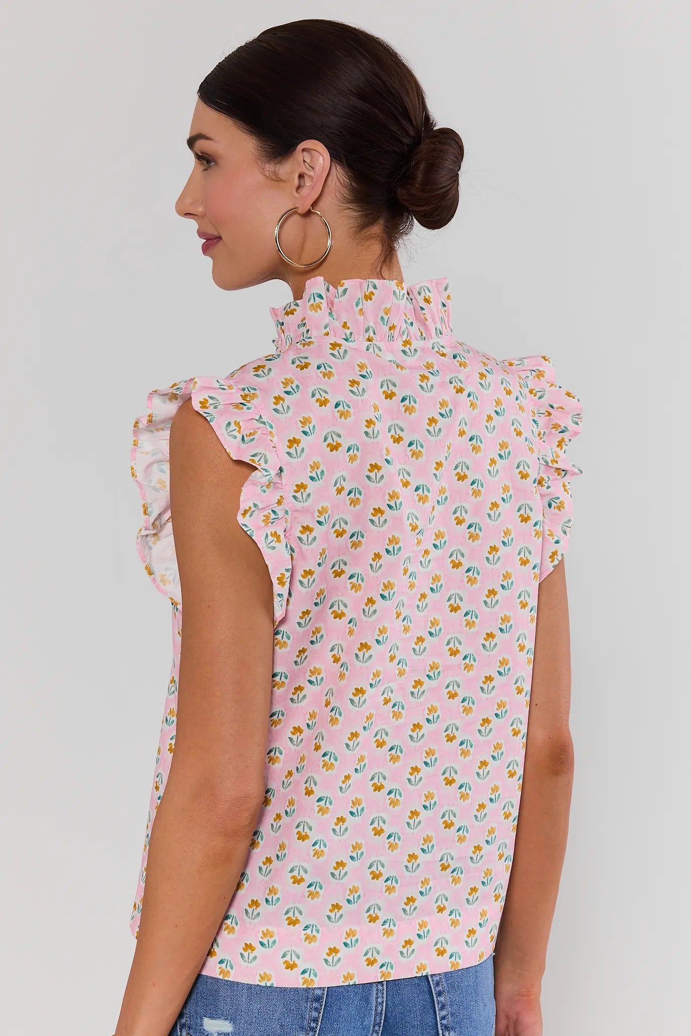 Woman wearing a pink floral sleeveless top against a plain background standing