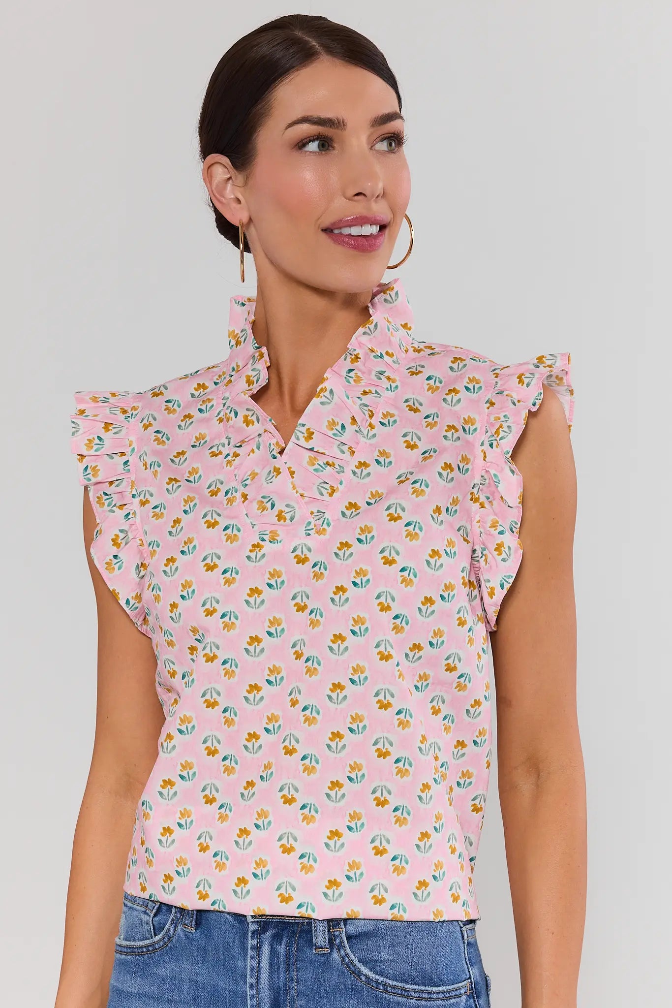 Woman standing wearing a pink floral sleeveless blouse against a plain background