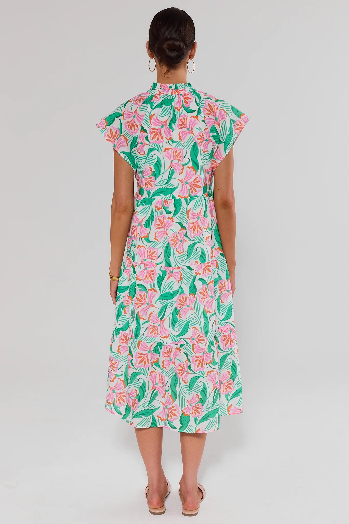 Woman standing wearing a floral dress with a plain background