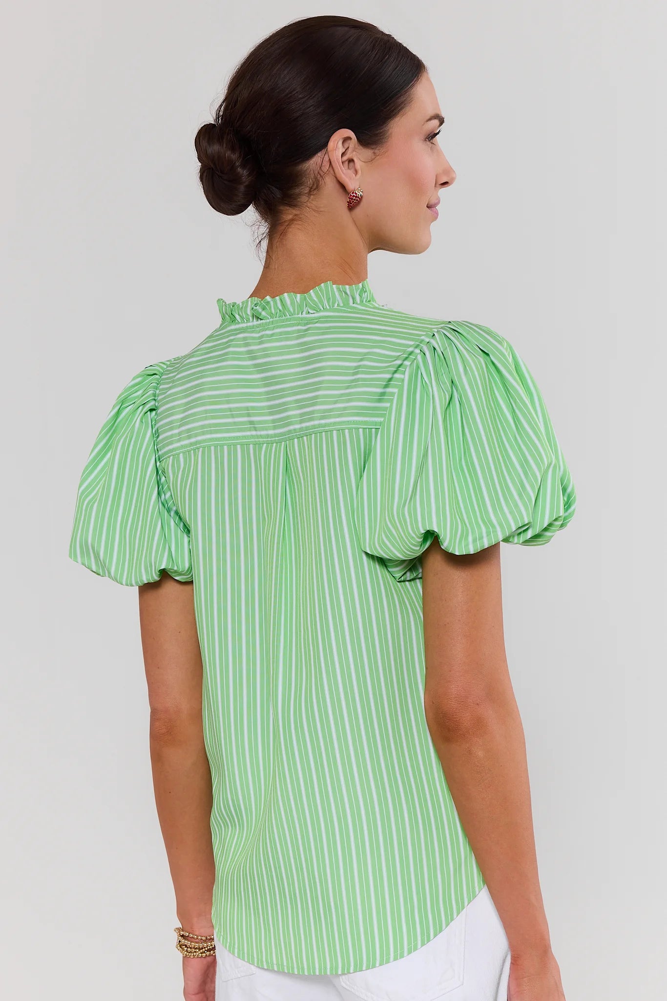 Woman standing wearing a green and white striped blouse against a plain background