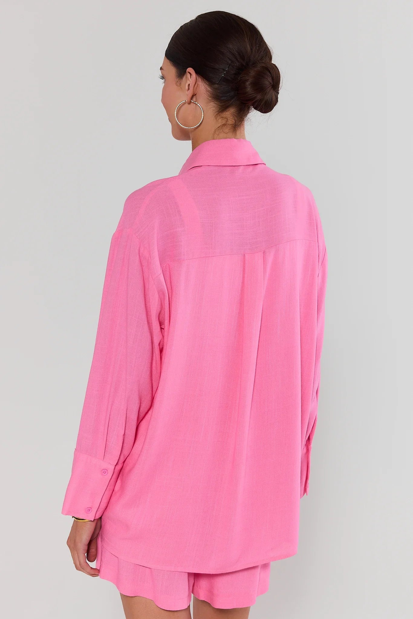 Person standing wearing a pink outfit with a matching shirt and shorts on a plain background