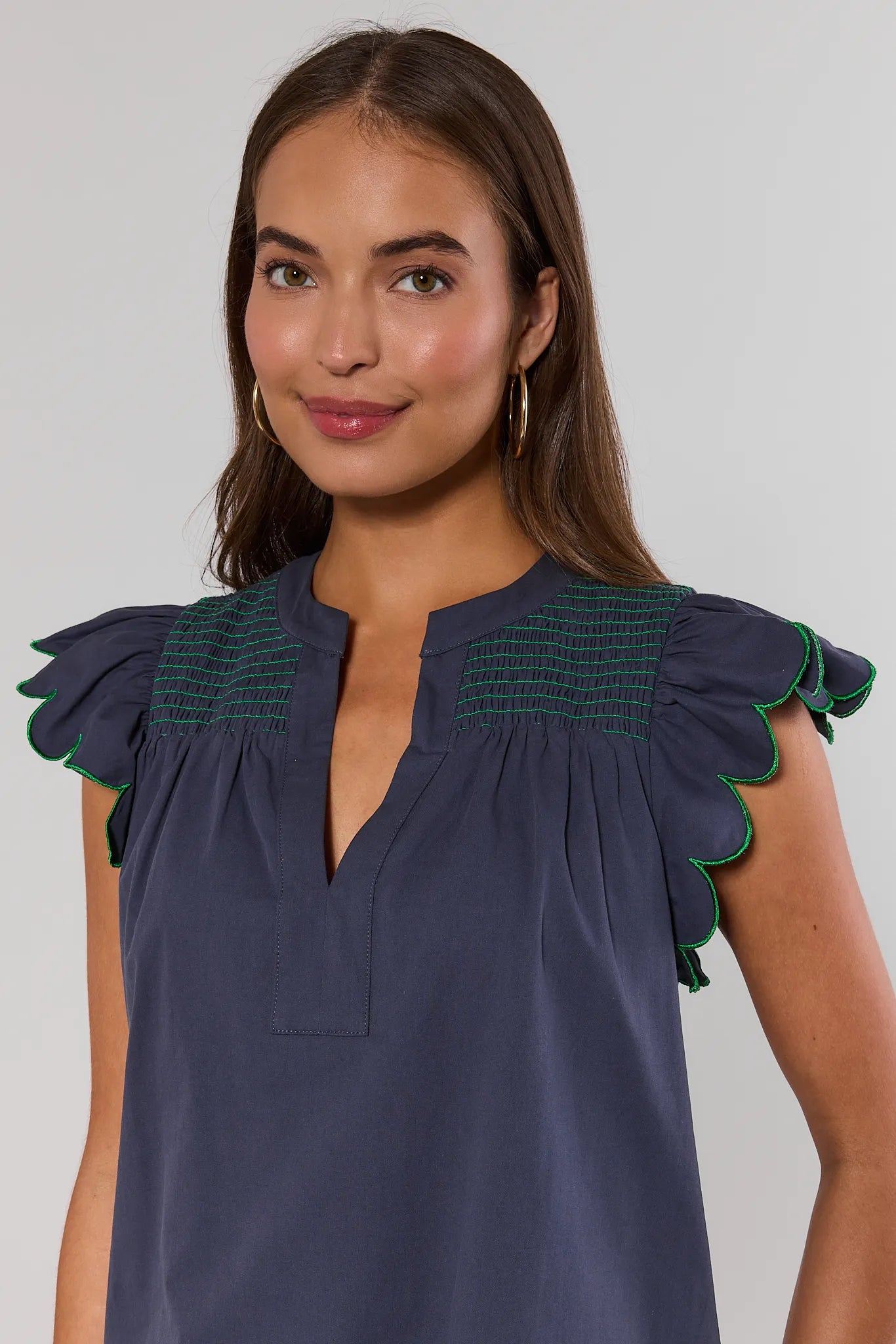 close up Woman wearing a dark blue blouse with green trim on a plain background