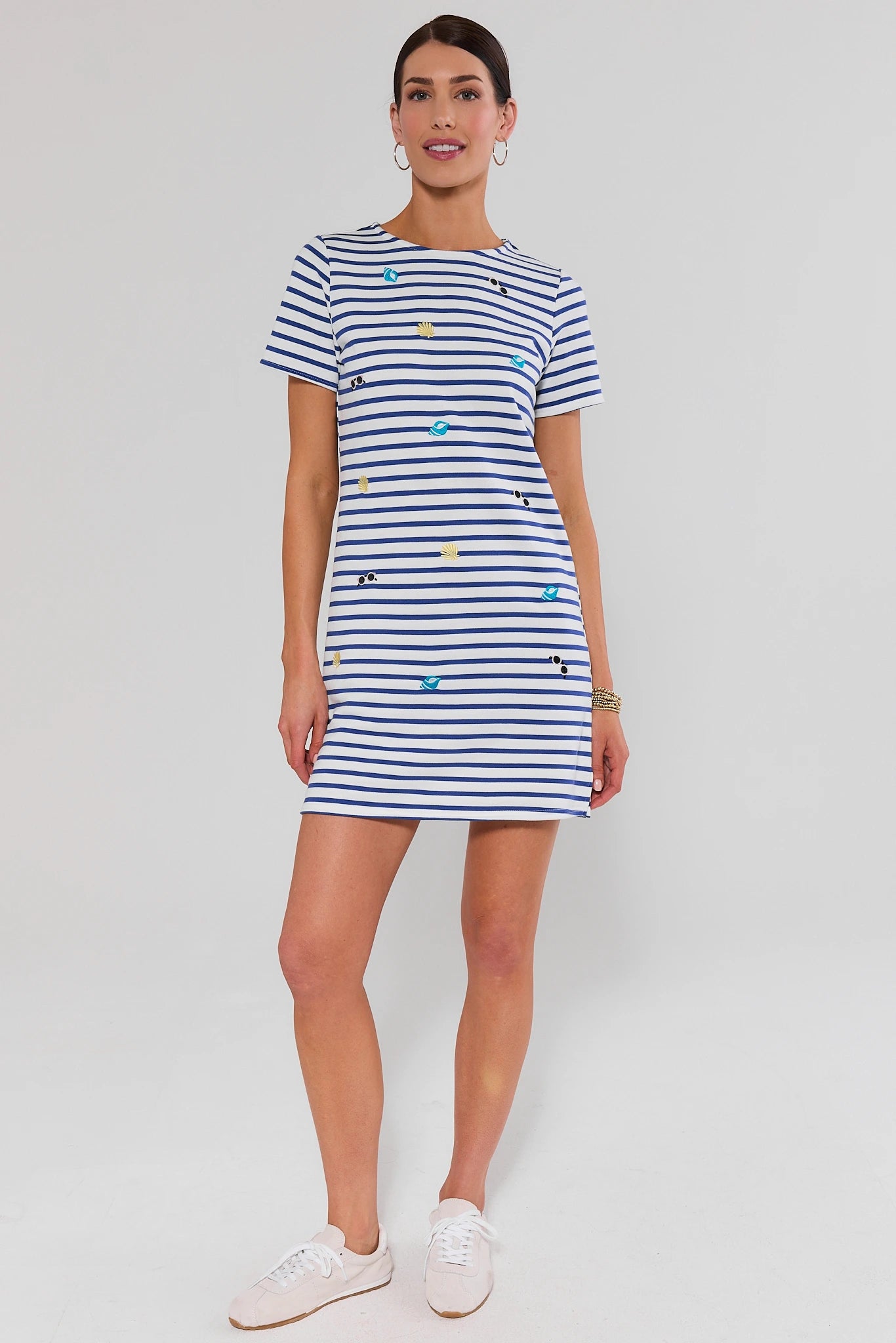 Woman standing wearing a blue and white striped dress with embroidered details on a plain background