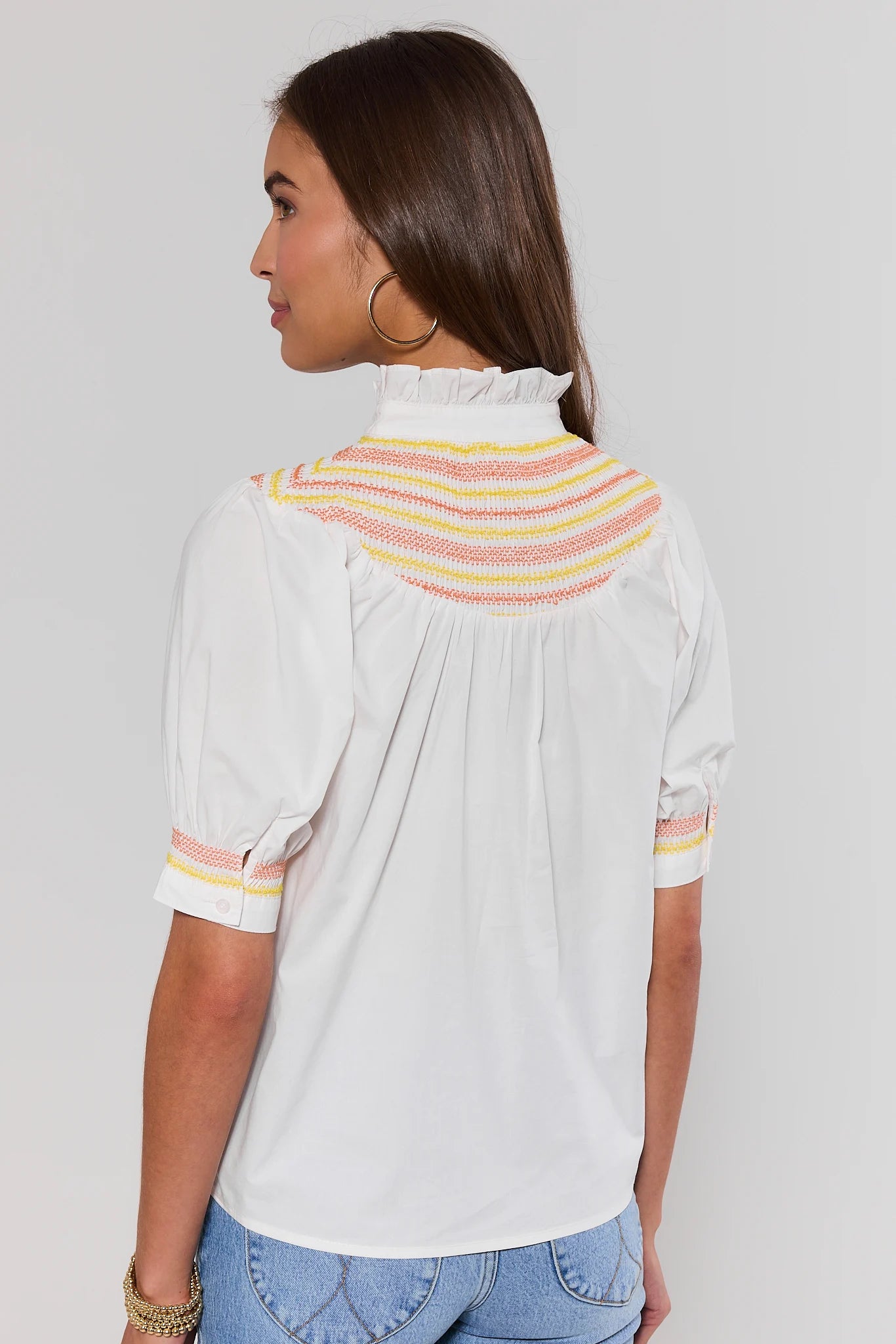 Woman wearing a white blouse with colorful accents on a plain background standing